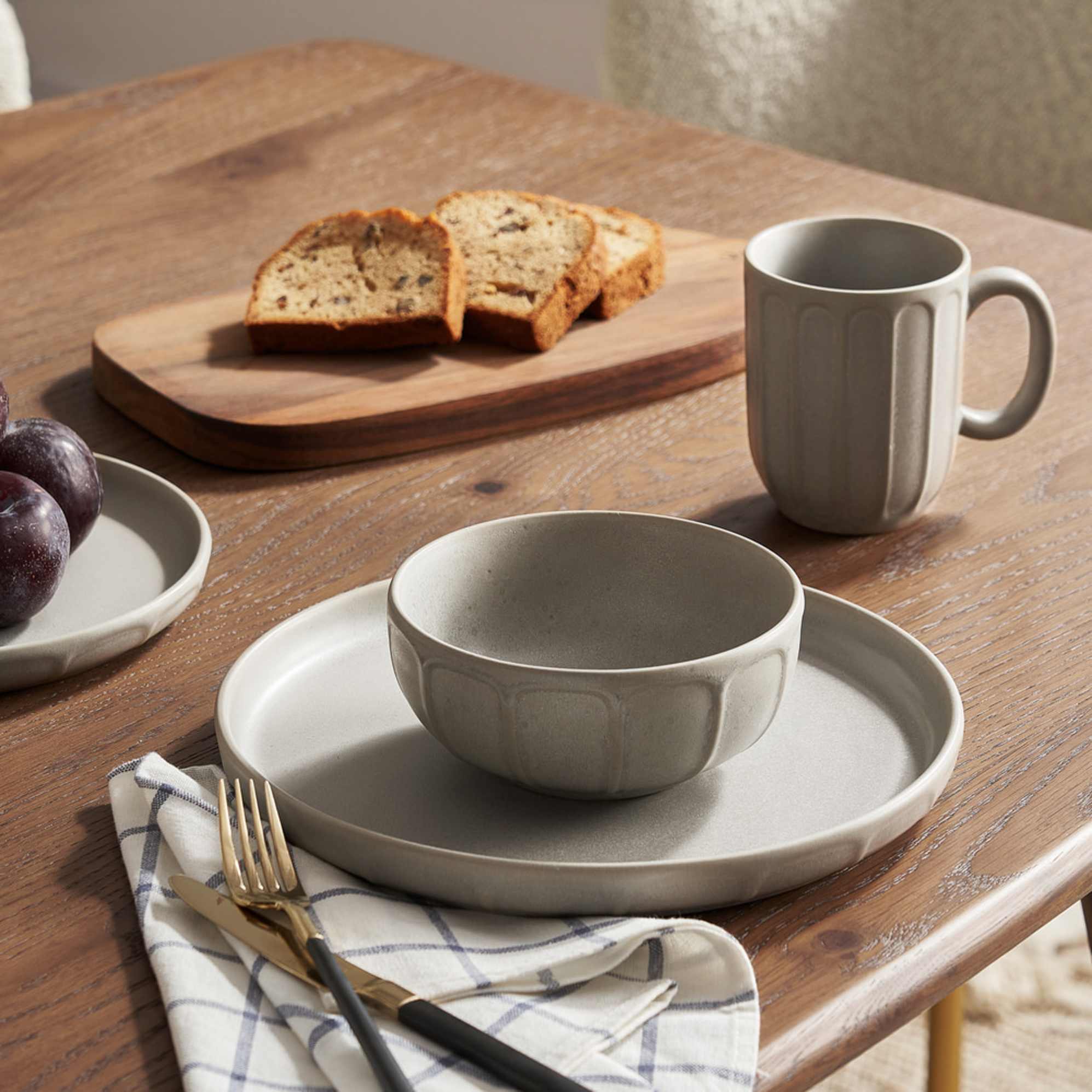A pottery bowl, plate, and matching mug placed on a wooden dining table.