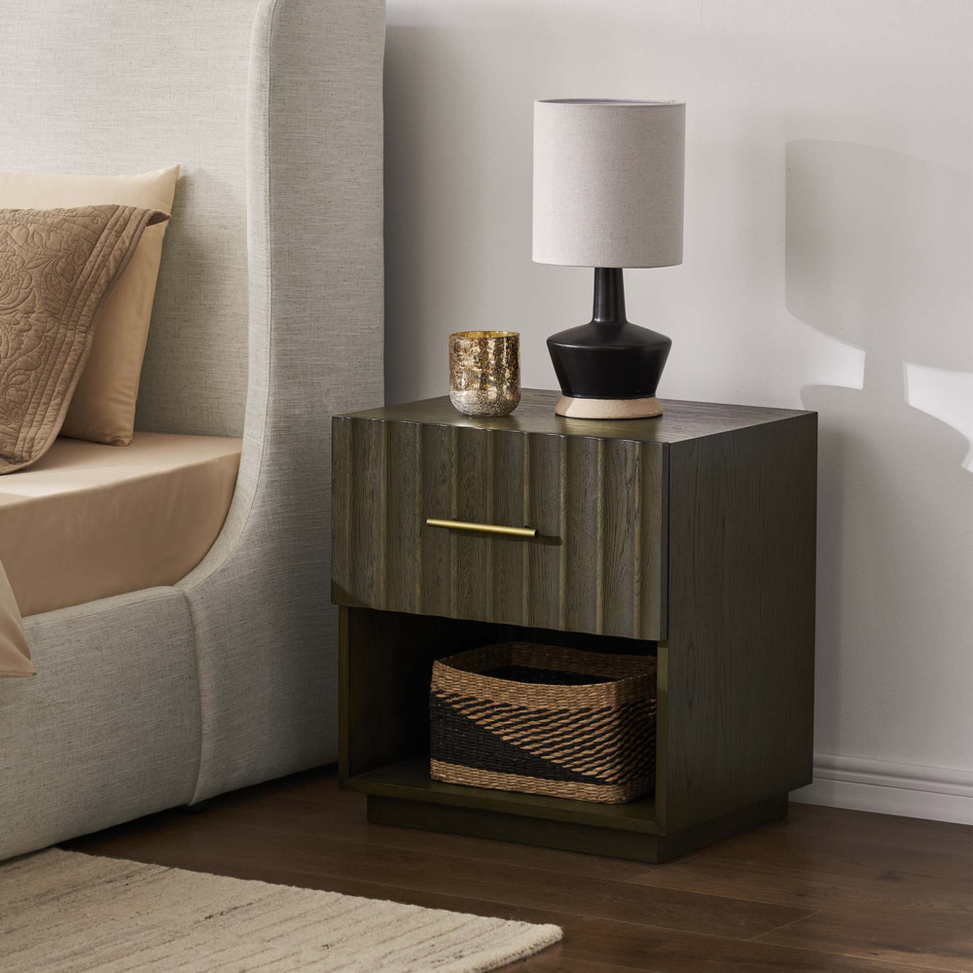 A dark-colored bedside table with a lamp and candle atop.