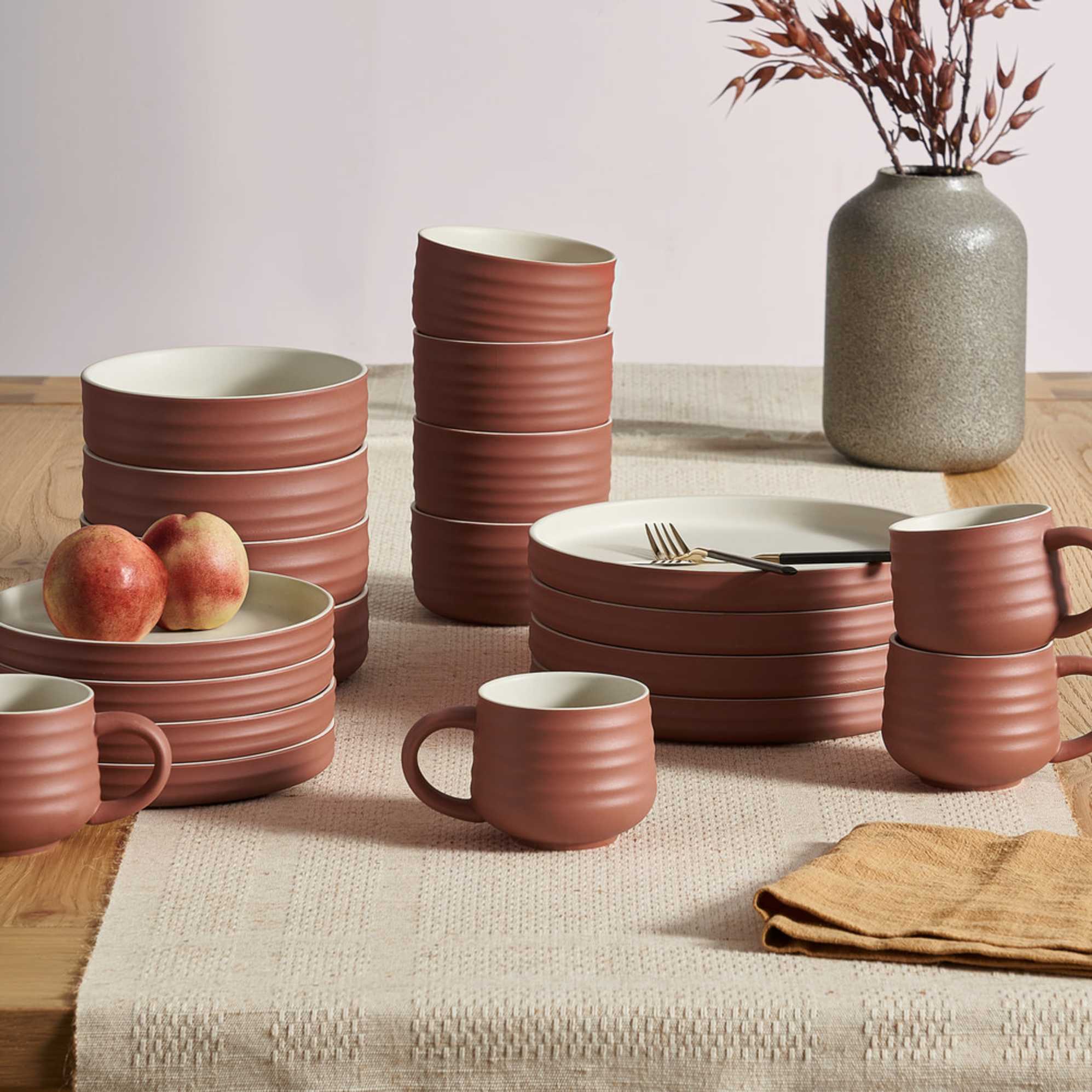 A brick red dinnerware set with plates, bowls, and mugs.