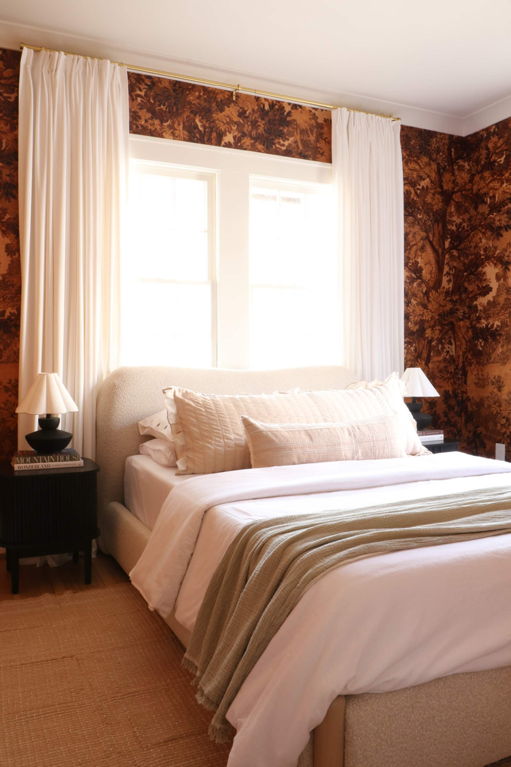 A bed placed against a window with sheer curtains draping beside it.