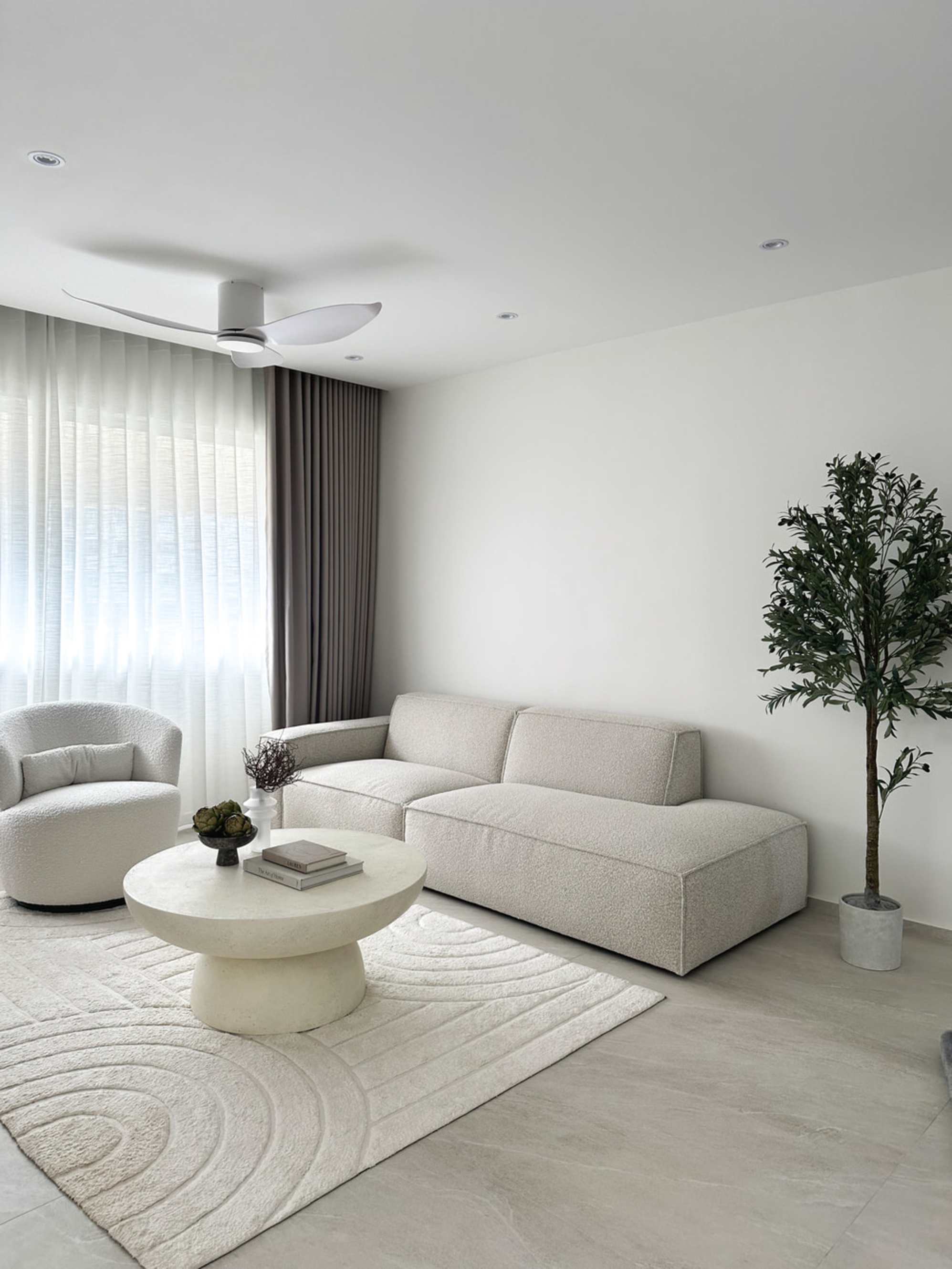 A white chaise sectional sofa, swivel chair, and round coffee table in a living room with white walls.