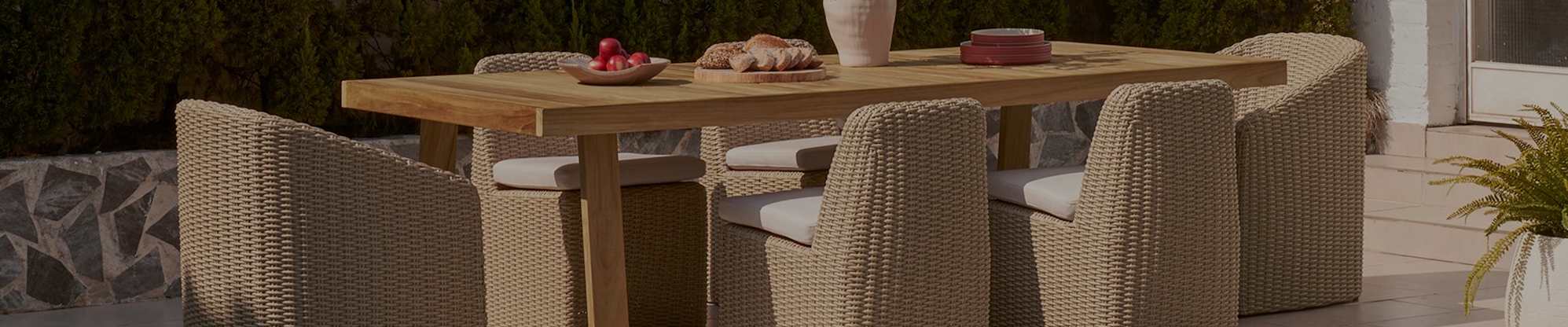 Six wicker outdoor dining chairs and a teak outdoor dining table.