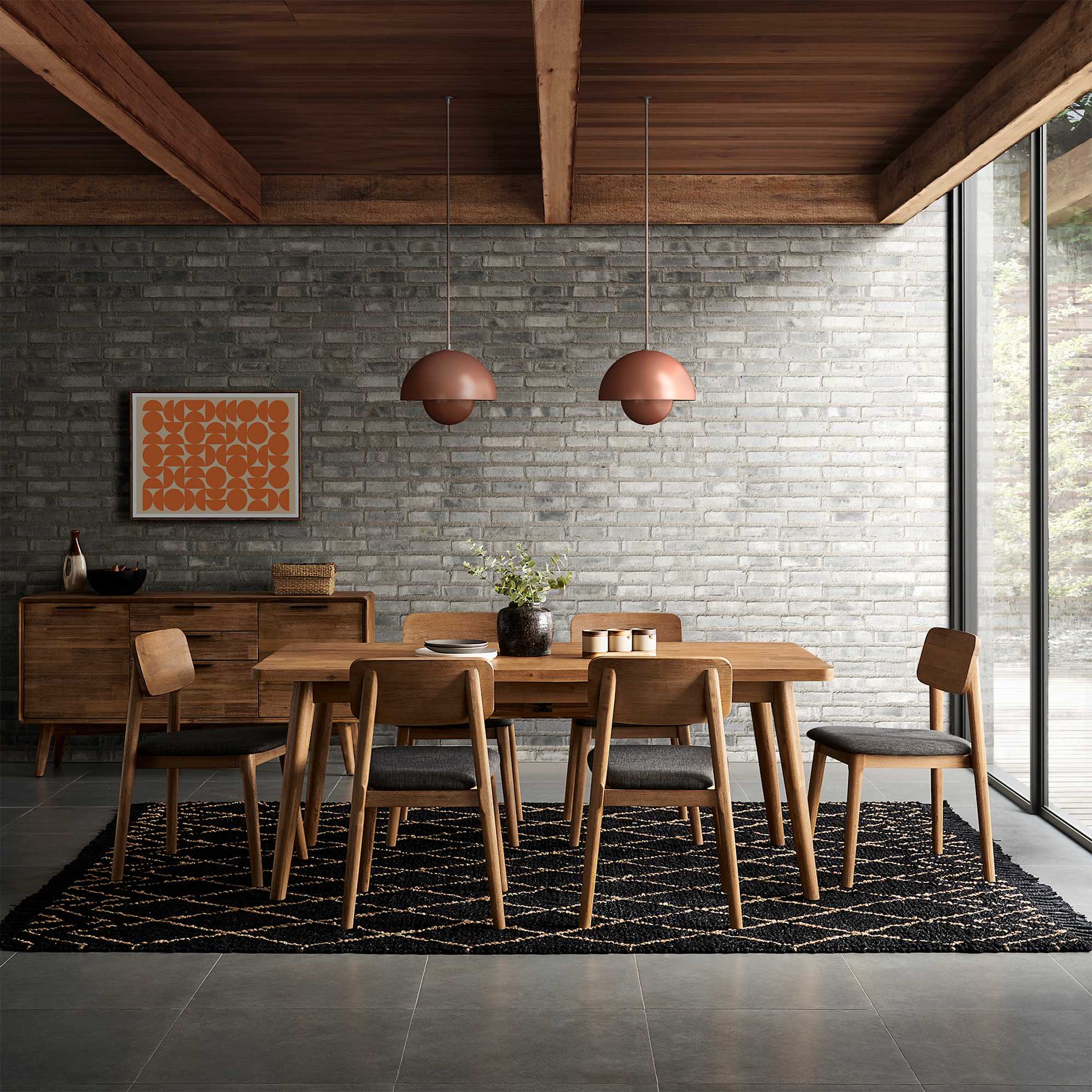 An acacia wood dining table and matching chairs atop a black rug.