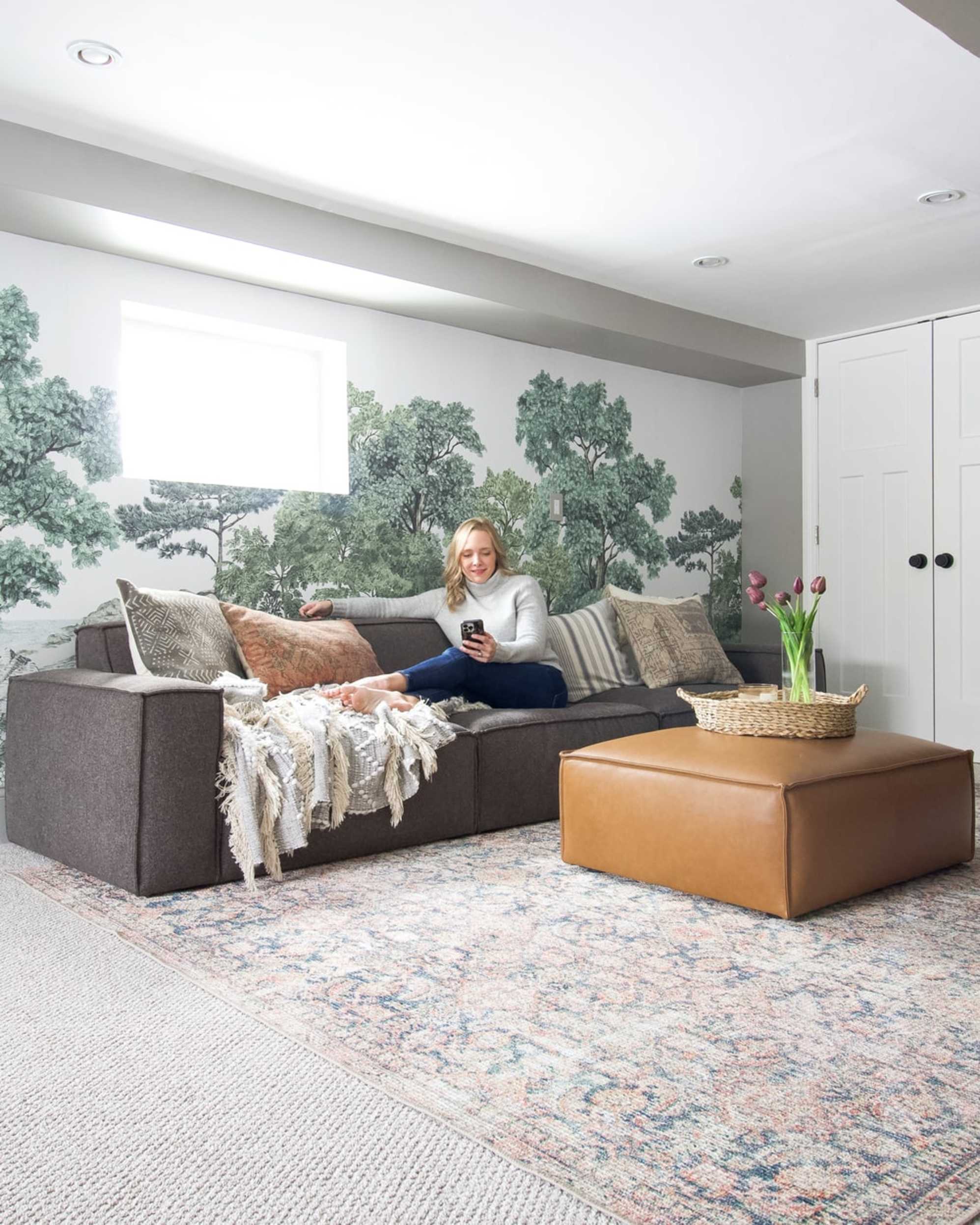 A person sitting on a black sofa with a leather ottoman in a living room.