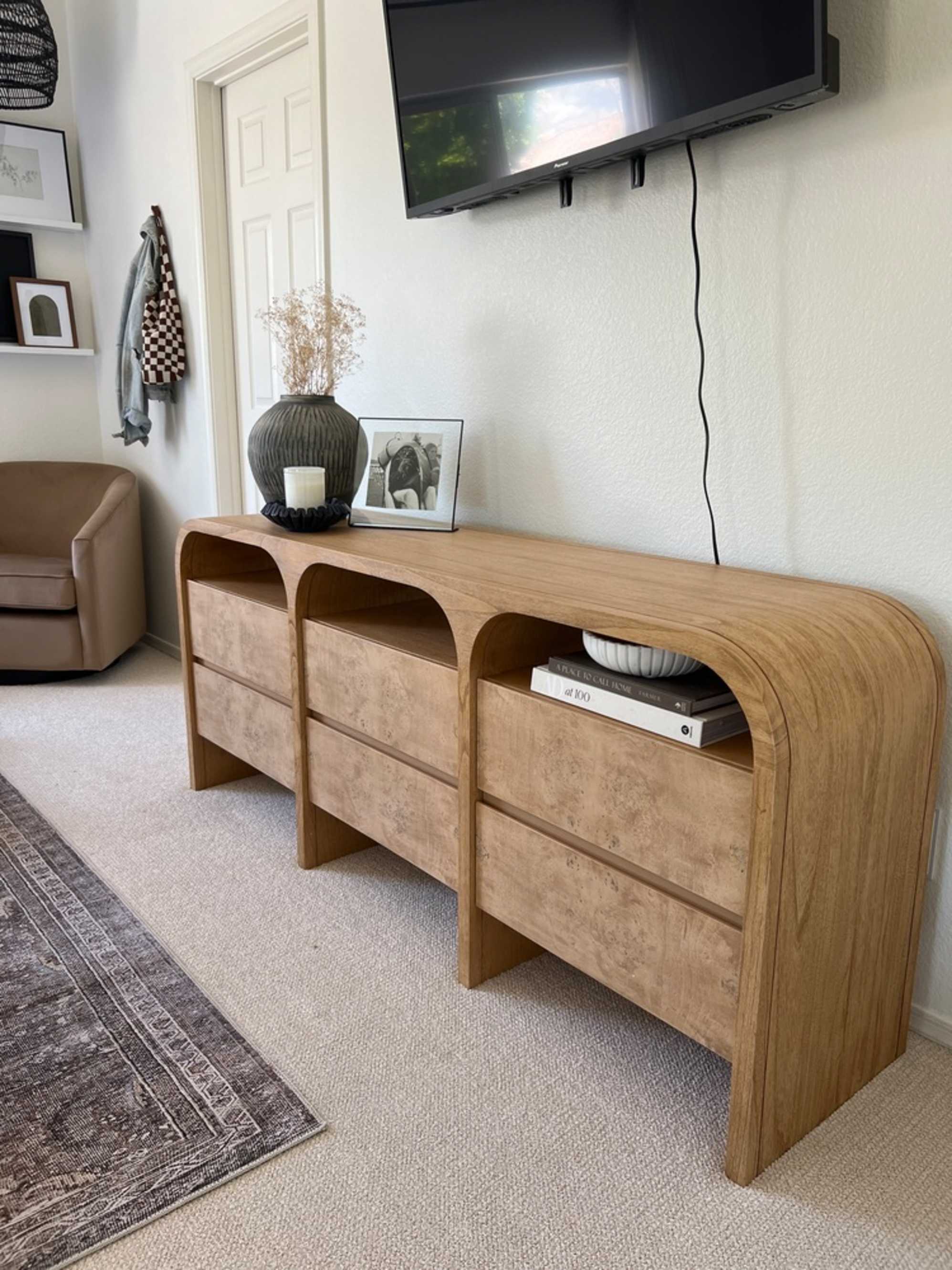 A wooden rounded dresser with a TV mounted on the wall behind it.