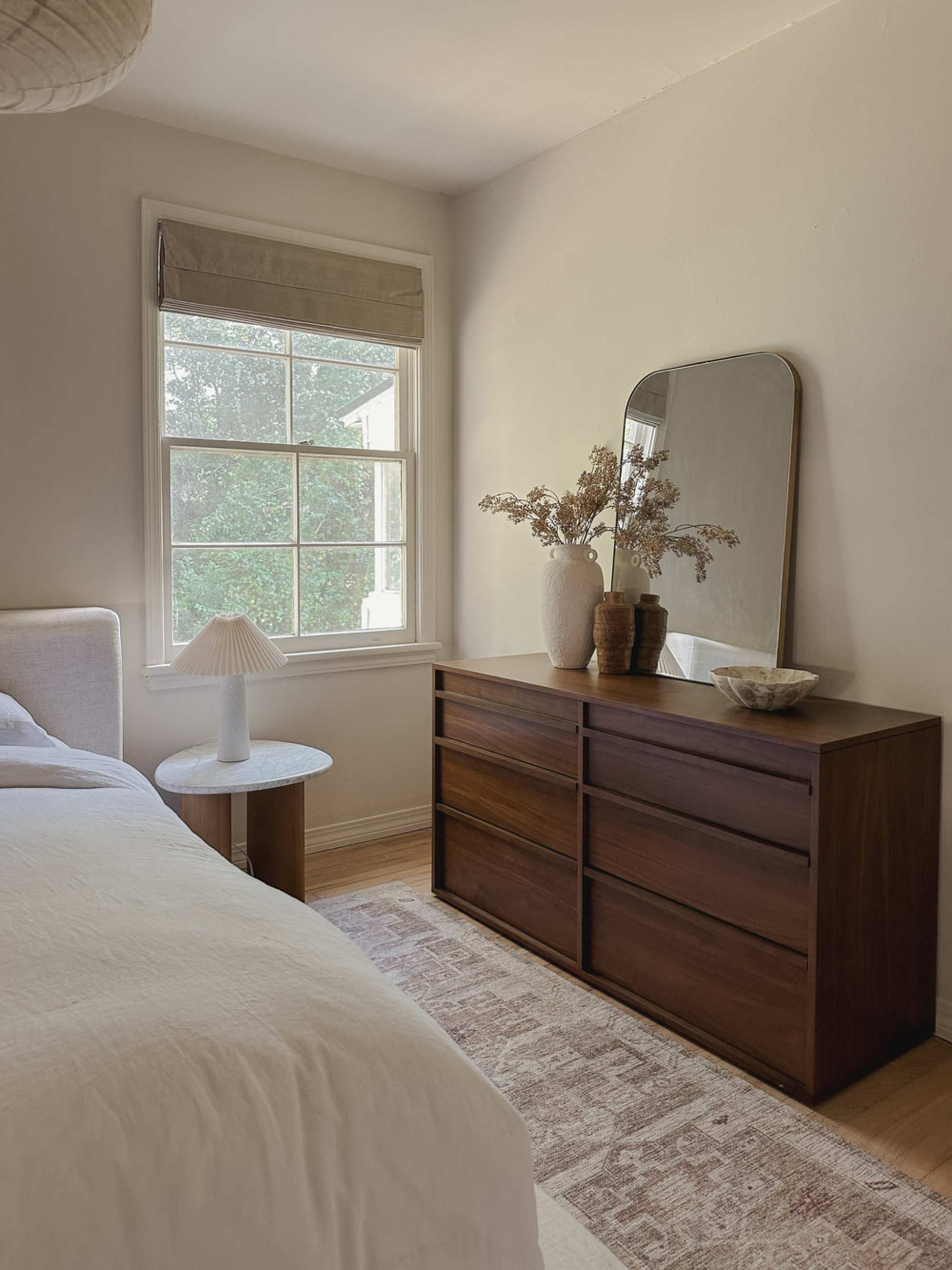 A wooden 6-drawer dresser with a mirror and two vases atop.