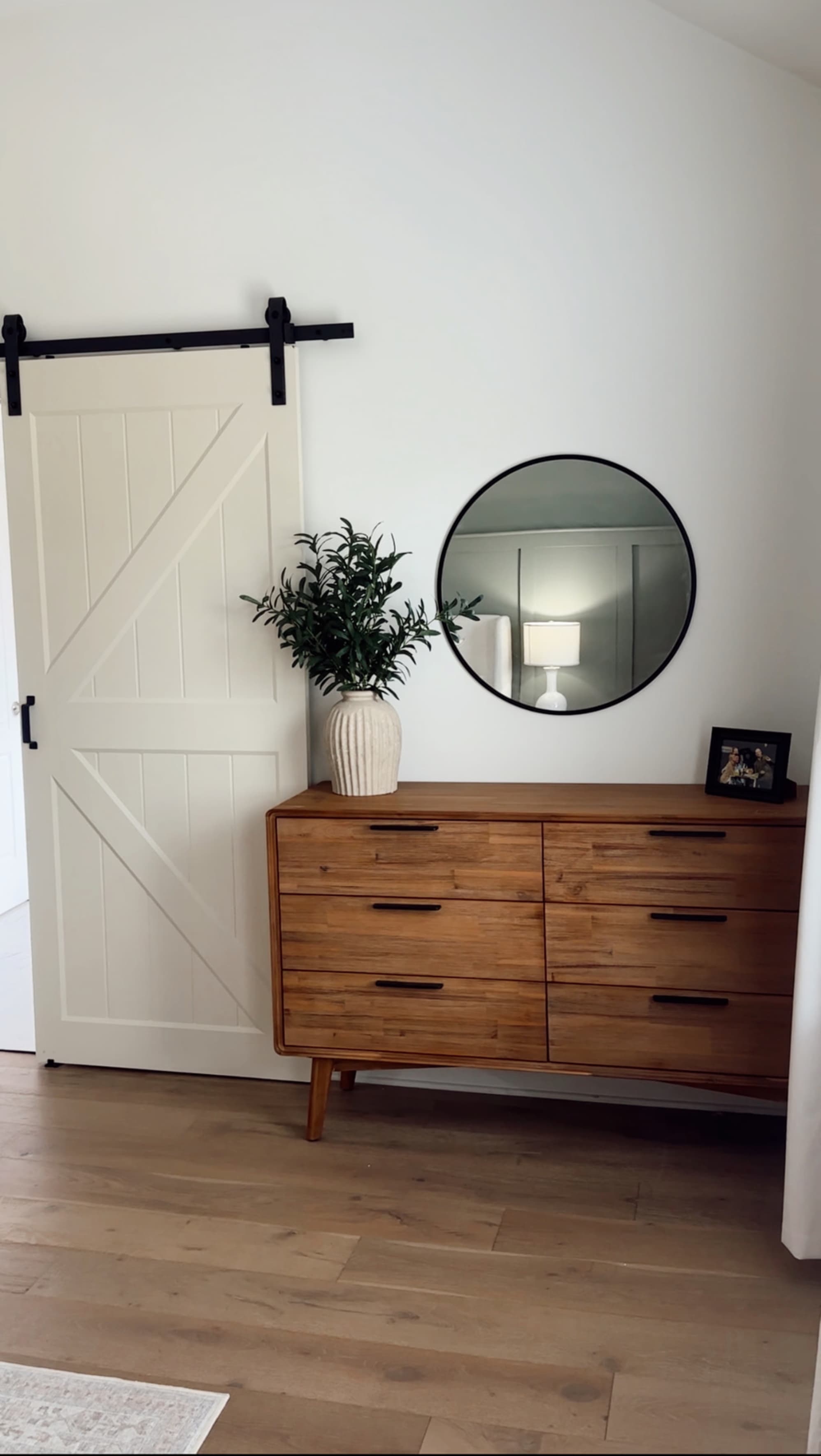An acacia wood 6-drawer dresser placed in the corner of a bedroom beside a barn door.