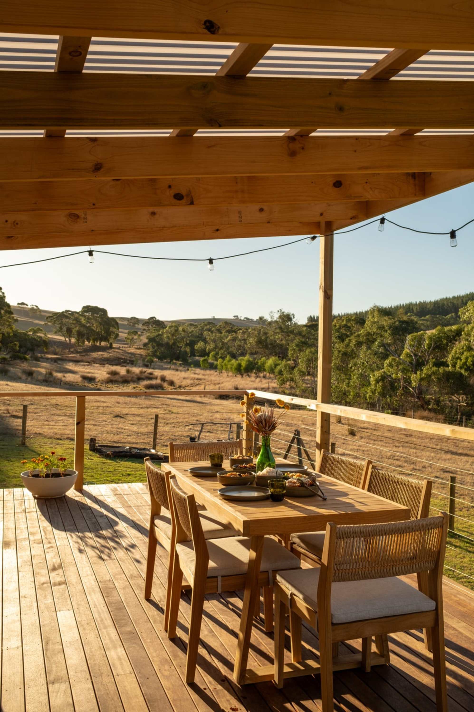 An outdoor teak dining table and chair set with tableware laid out on the table top.