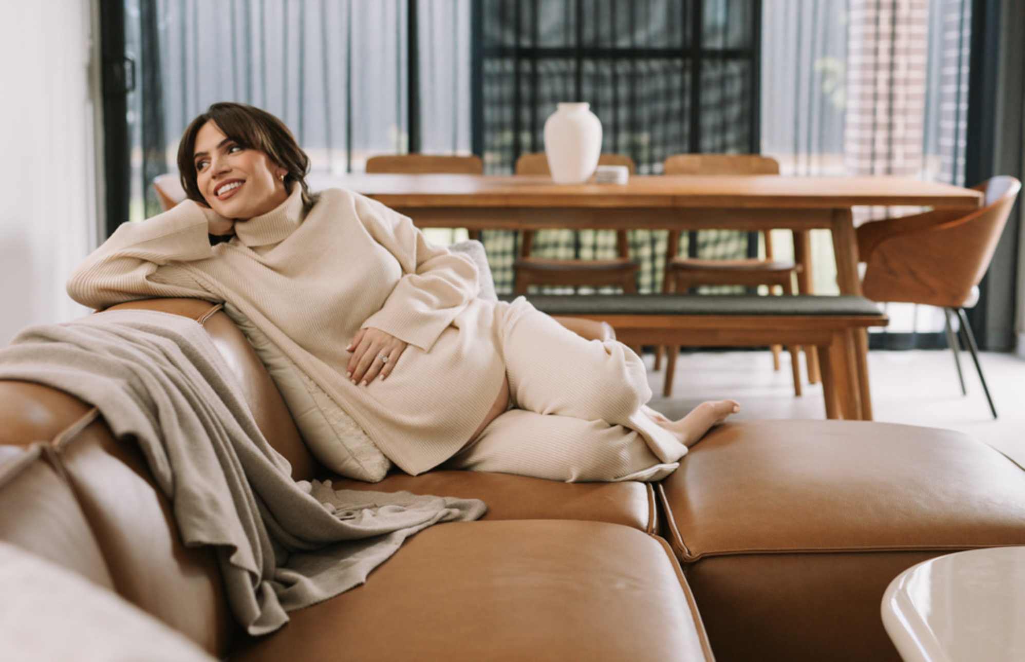 A person lying down on a leather sofa in a living room.