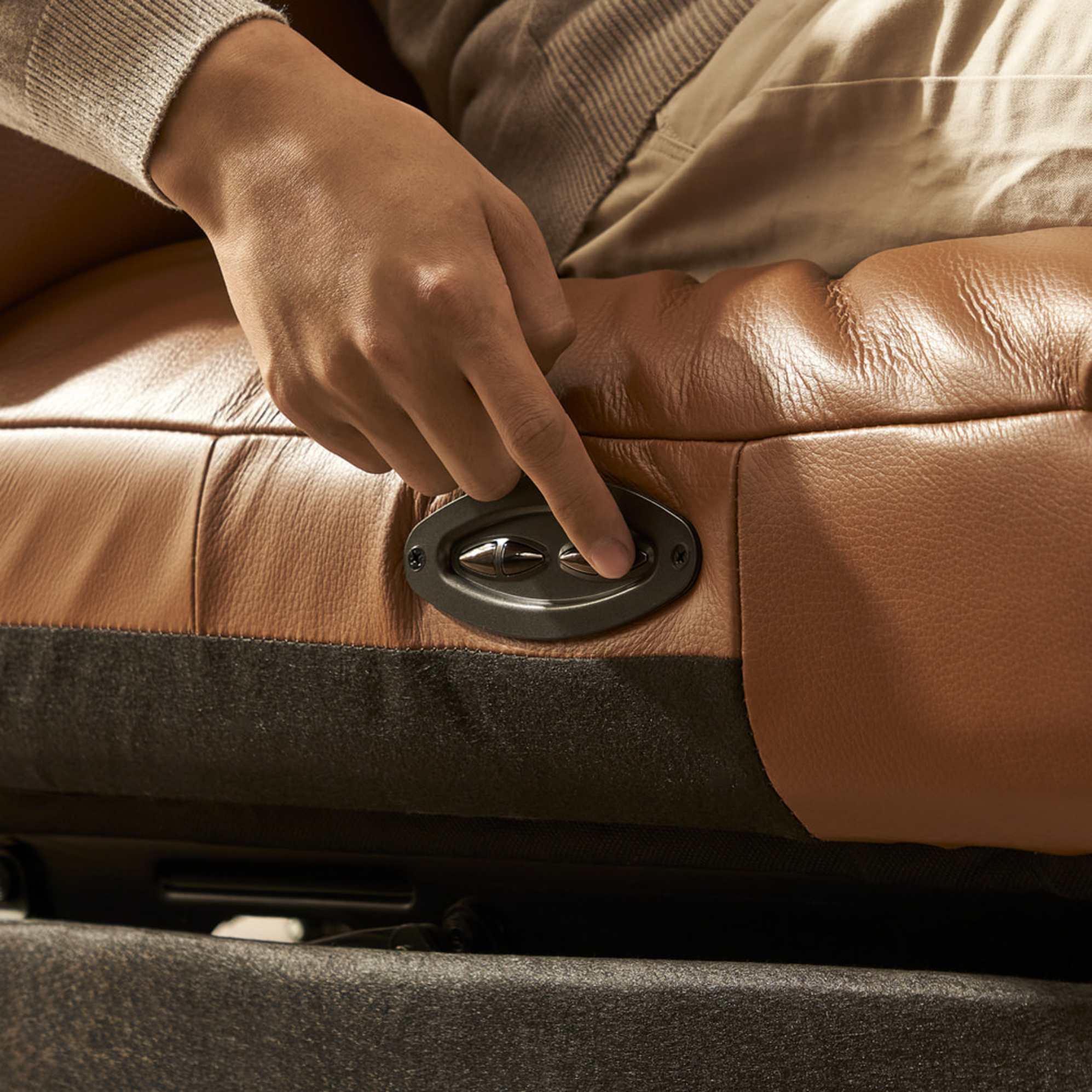 A person pressing a button on the controls of a power recliner. 