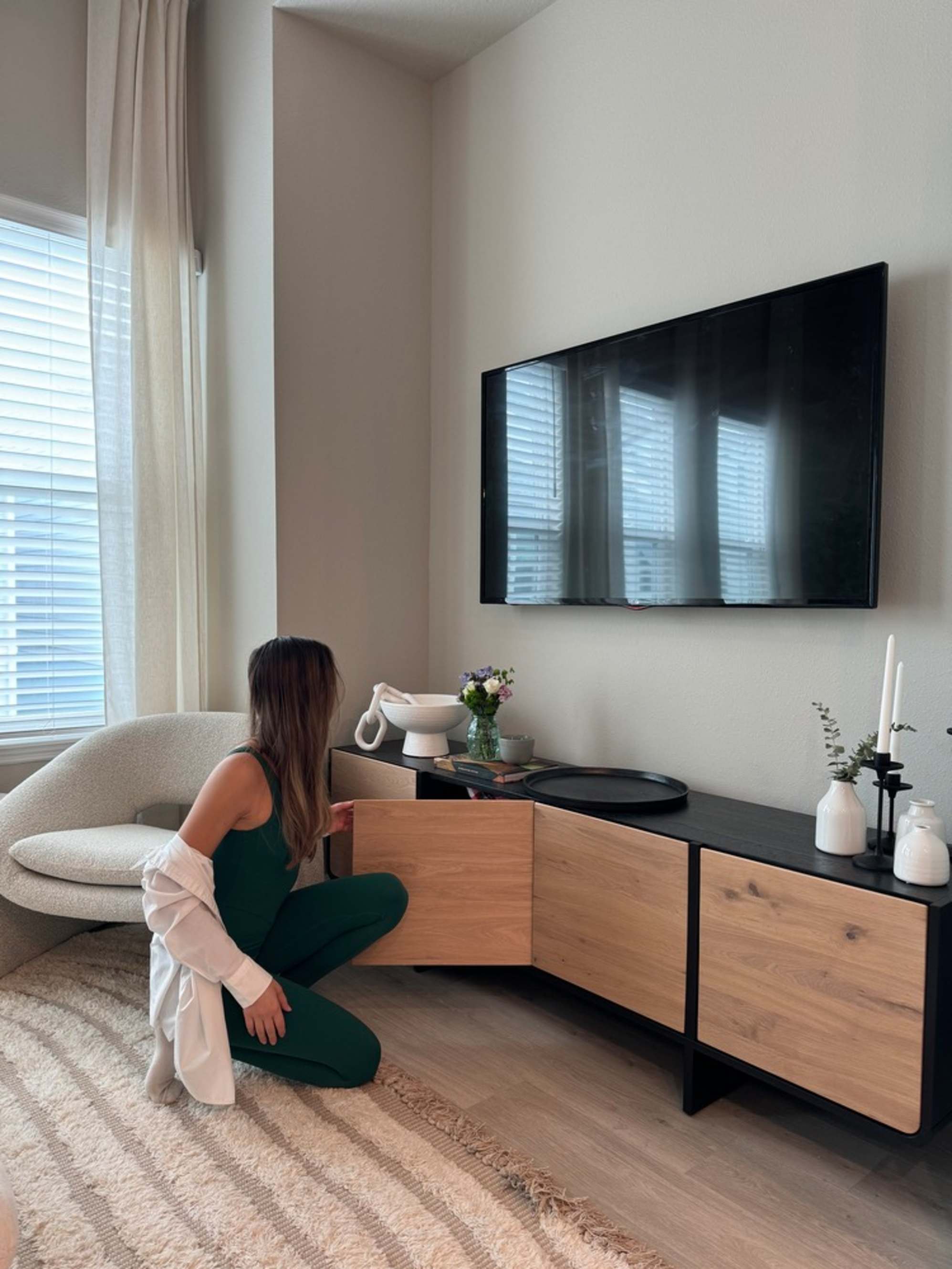 A person kneeling on the floor opening a cabinet door of a TV stand.