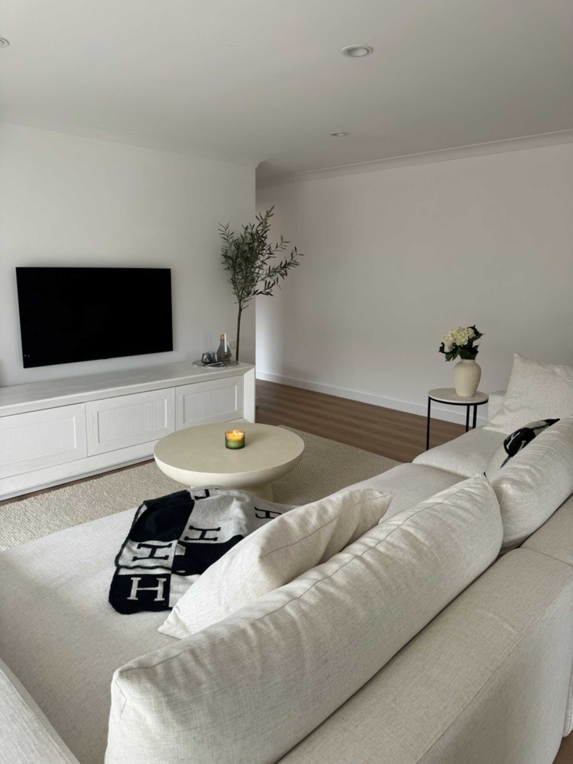 A wide chaise sectional sofa and white round coffee table placed infront of a wall-mounted TV.
