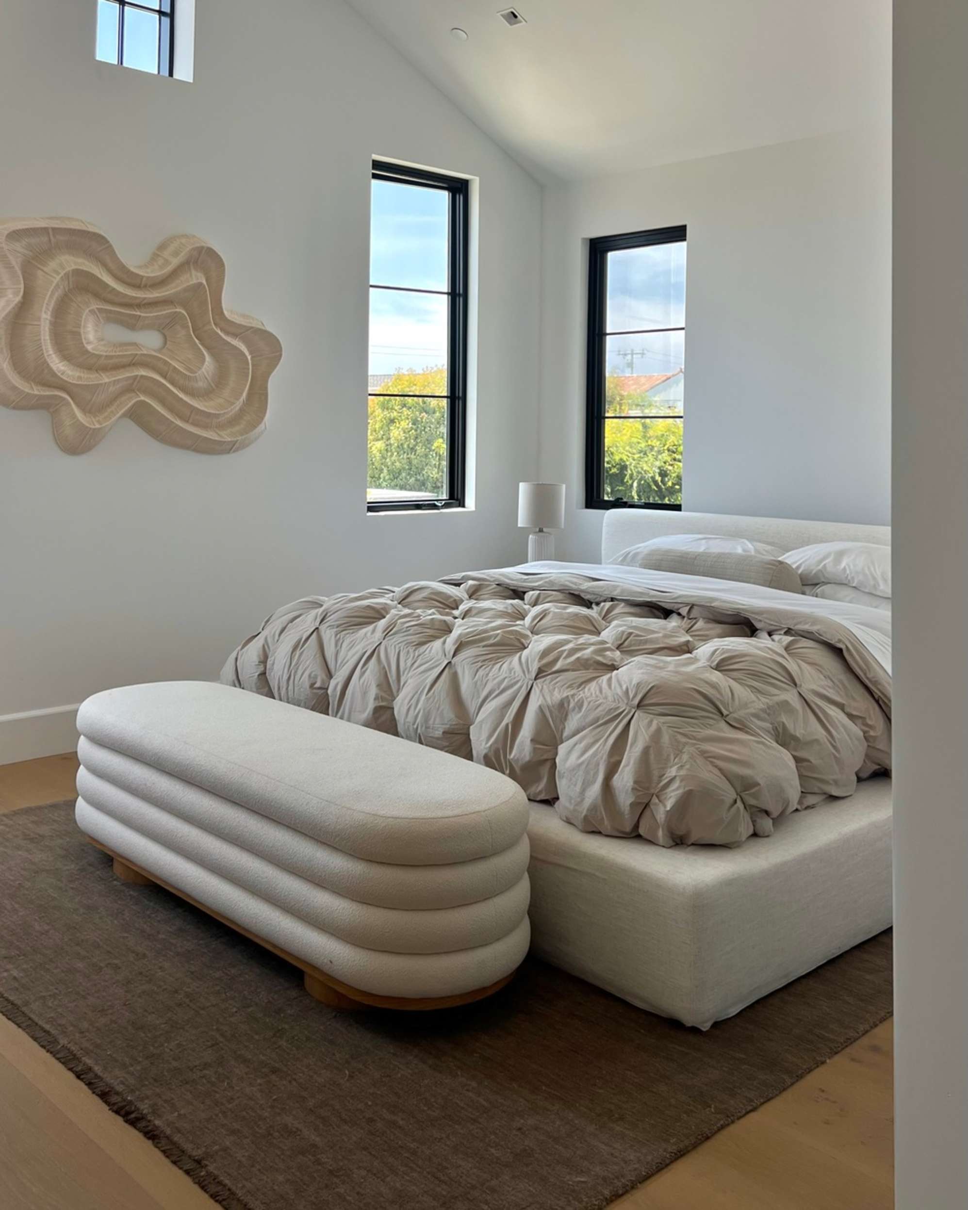 A storage bench placed infront of a bed with an area rug placed beneath it.