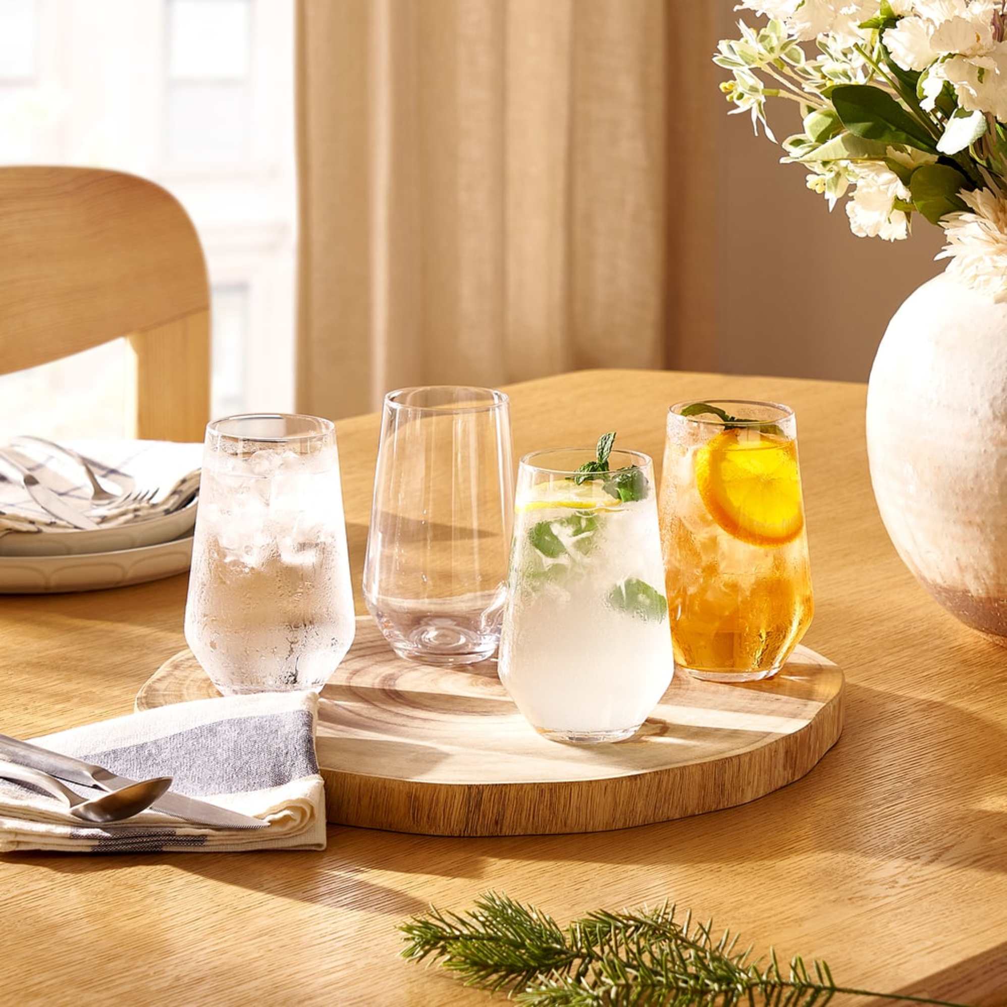 A set of four drinking glasses placed on a wooden plate charger.