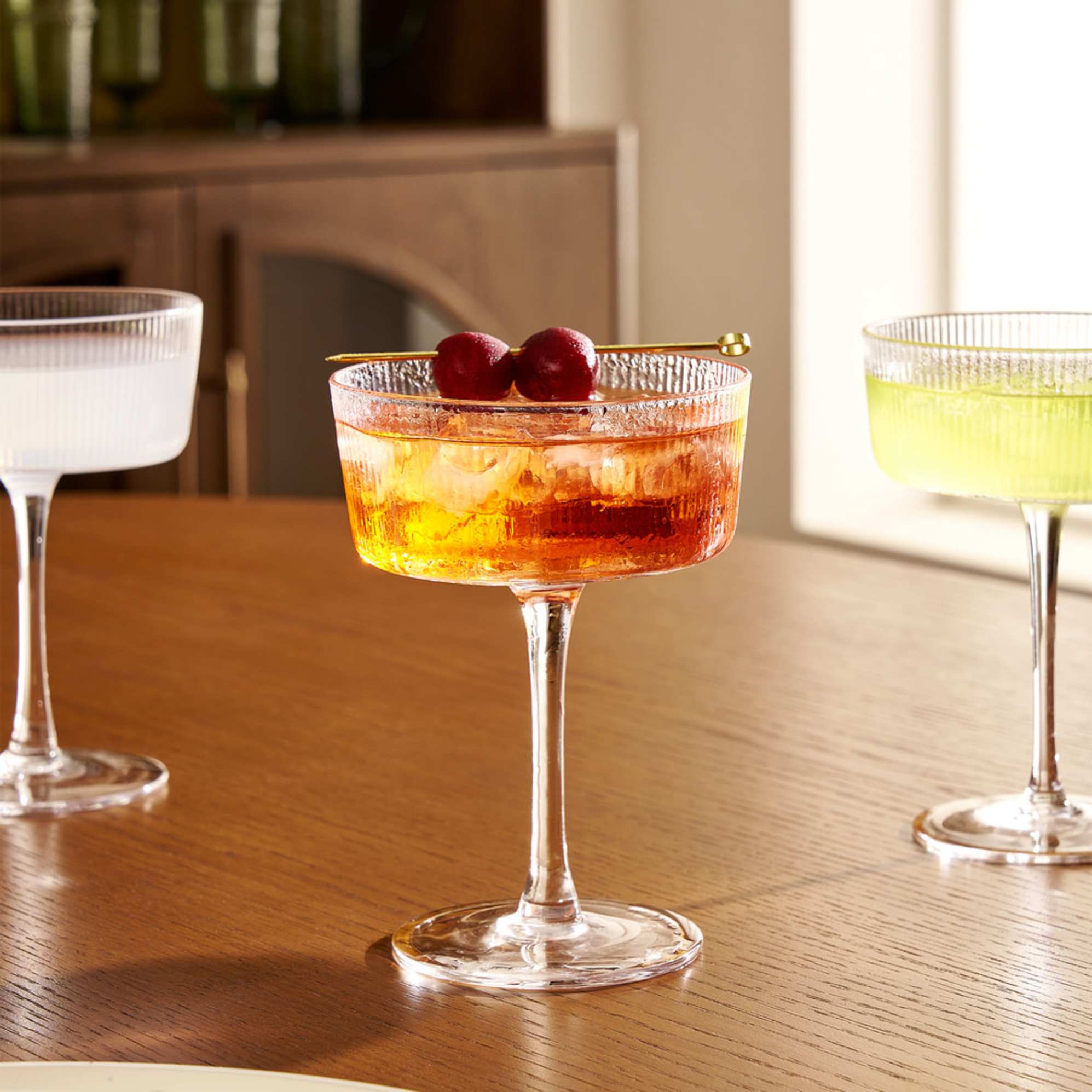A fluted coupe glass filled with a drink with cherries decorated on top.