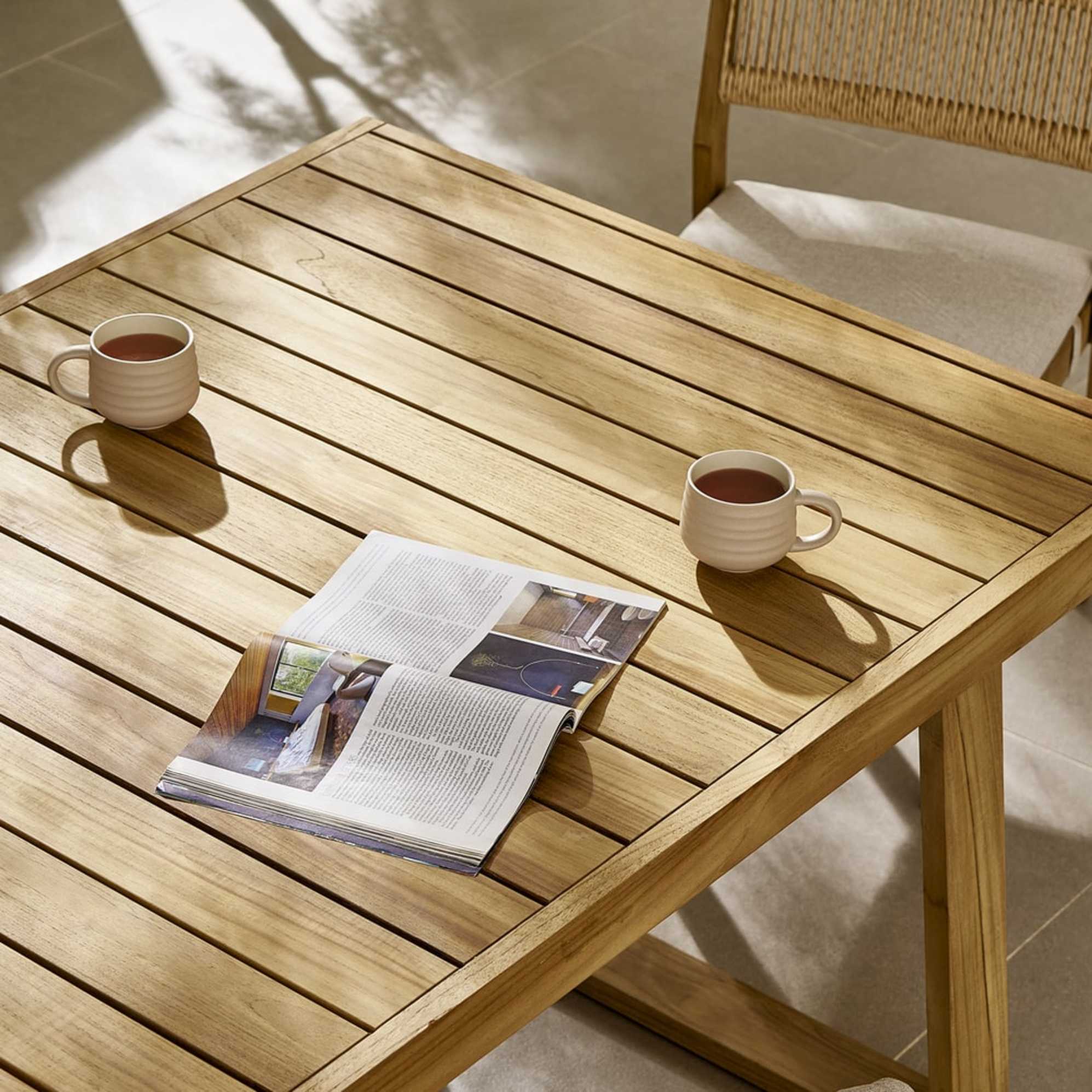A teak wood dining table with two coffee mugs.