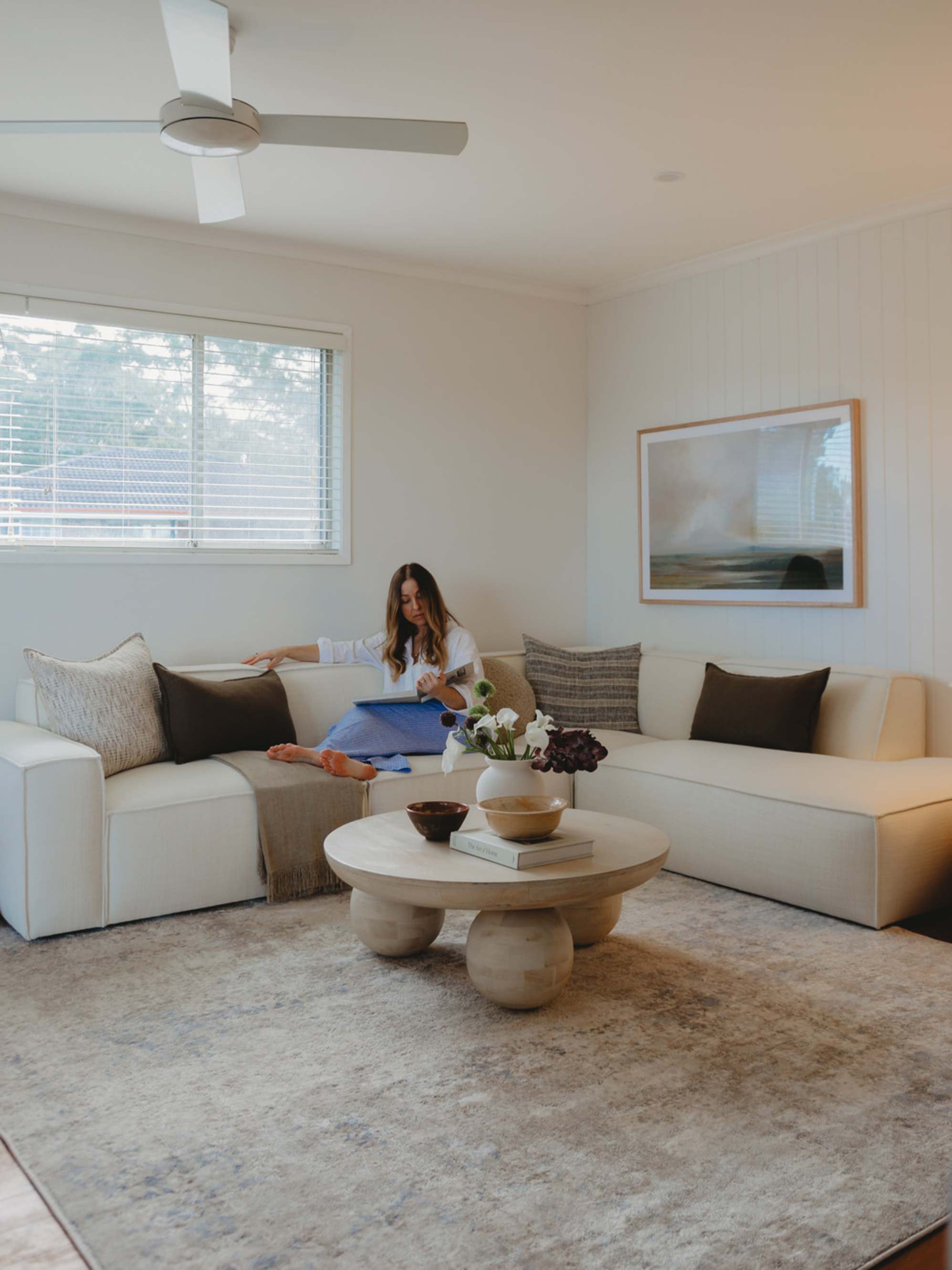 A person sitting on a white extended sofa in a living room.