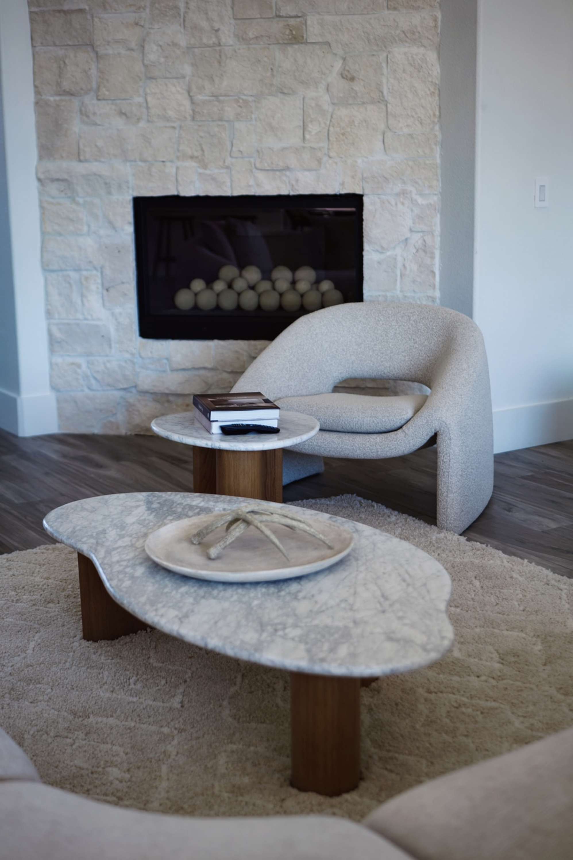 A low-slung armchair placed infront of a fireplace with a matching marble coffee and side table set.
