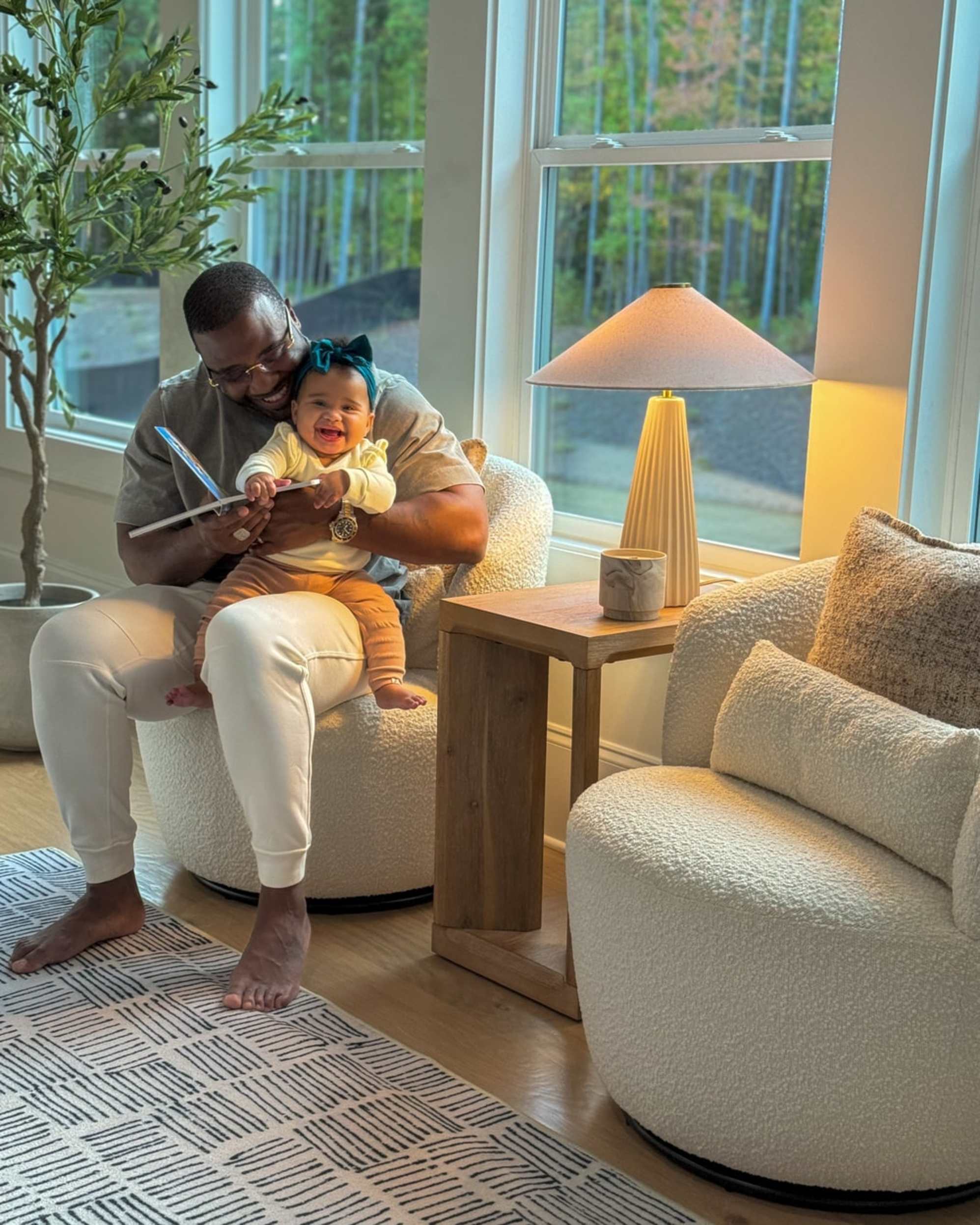 A man carrying a toddler while sitting on a rounded bouclé swivel chair.