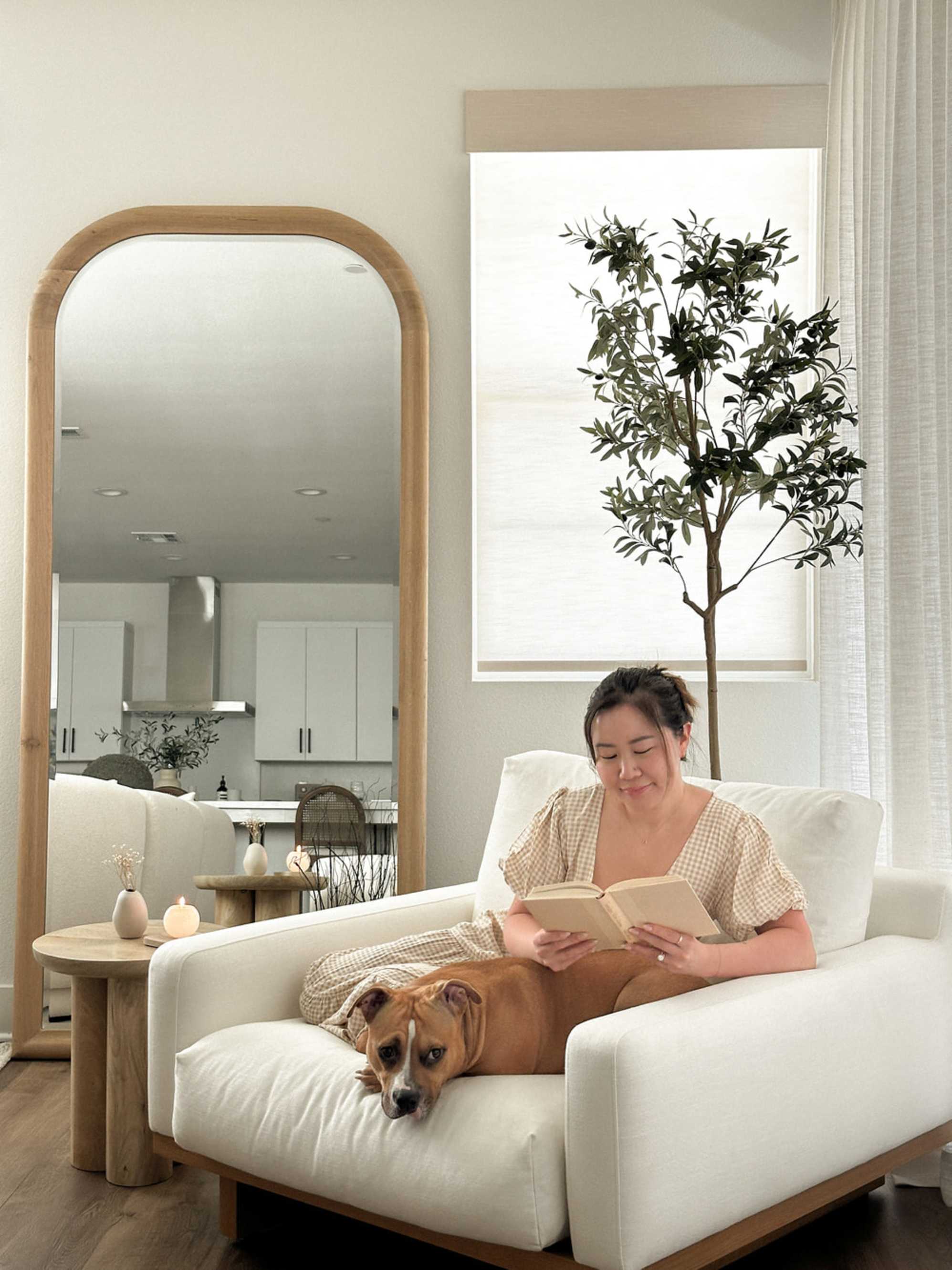 A person sitting on an armchair reading a book with their dog.