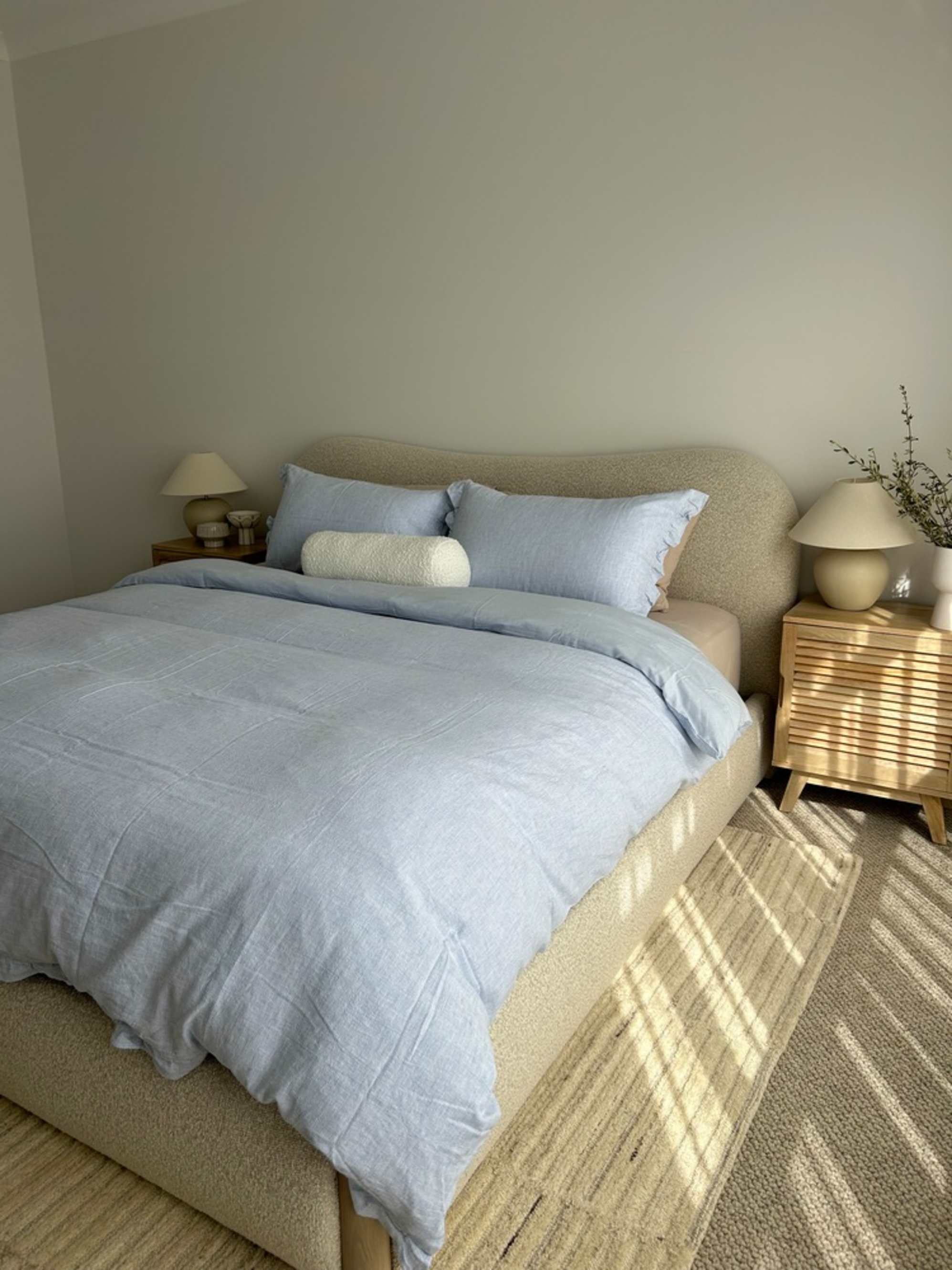 A performance fabric bed with light blue bedsheets and matching wooden nightstands.