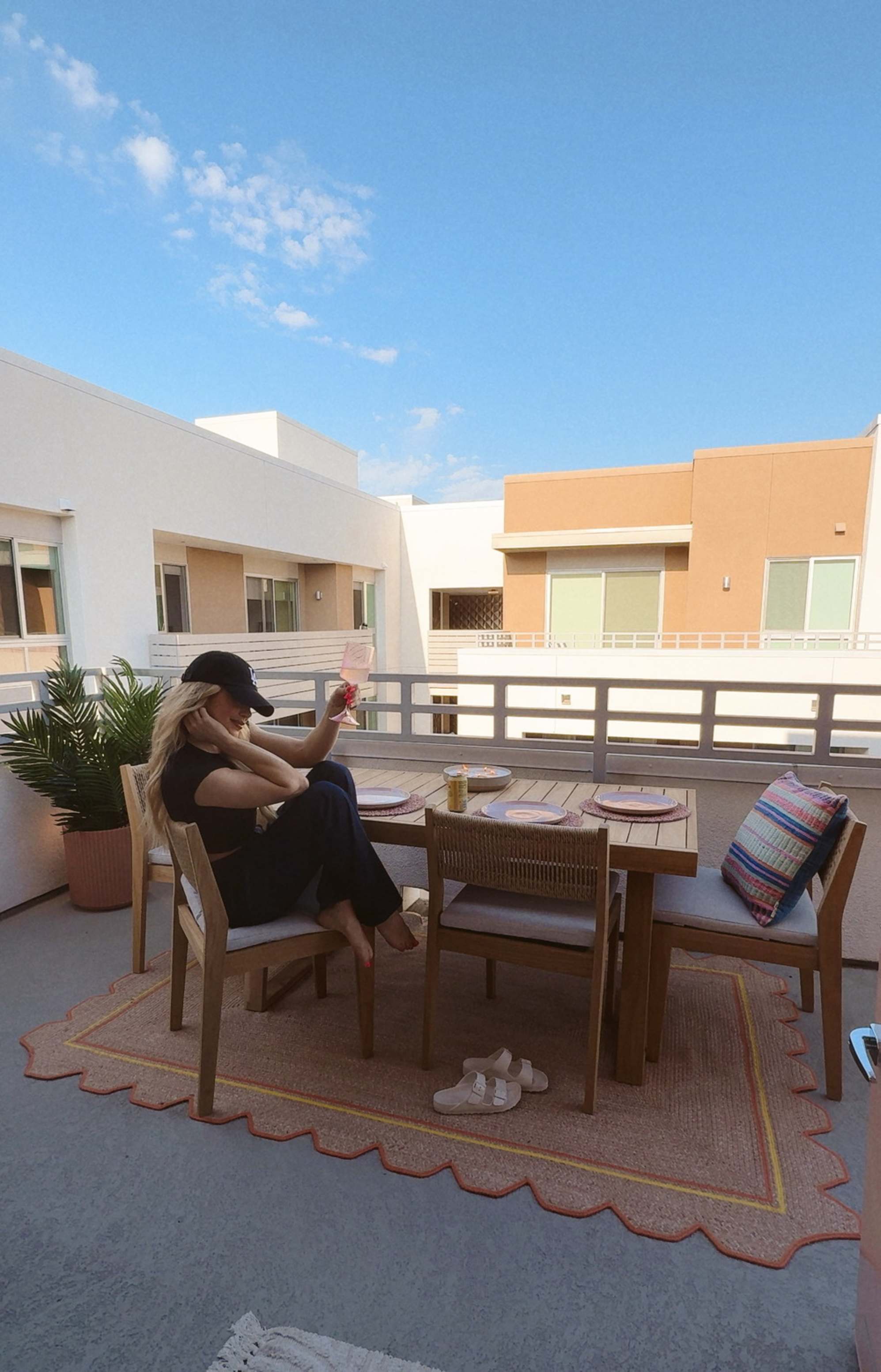 A person sitting on a teak outdoor dining chair holding a glass of drink.