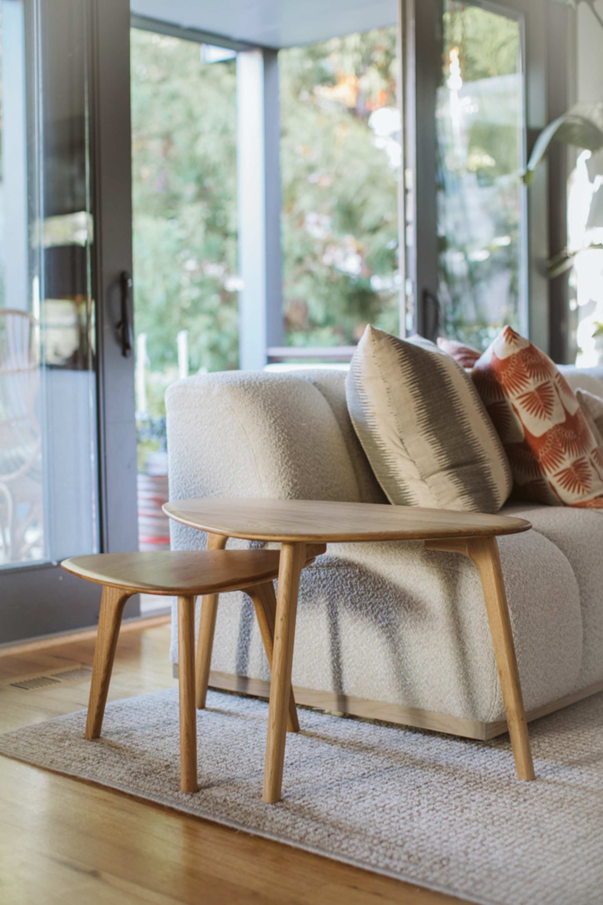 An oak wood nesting coffee table set is placed beside a sofa.