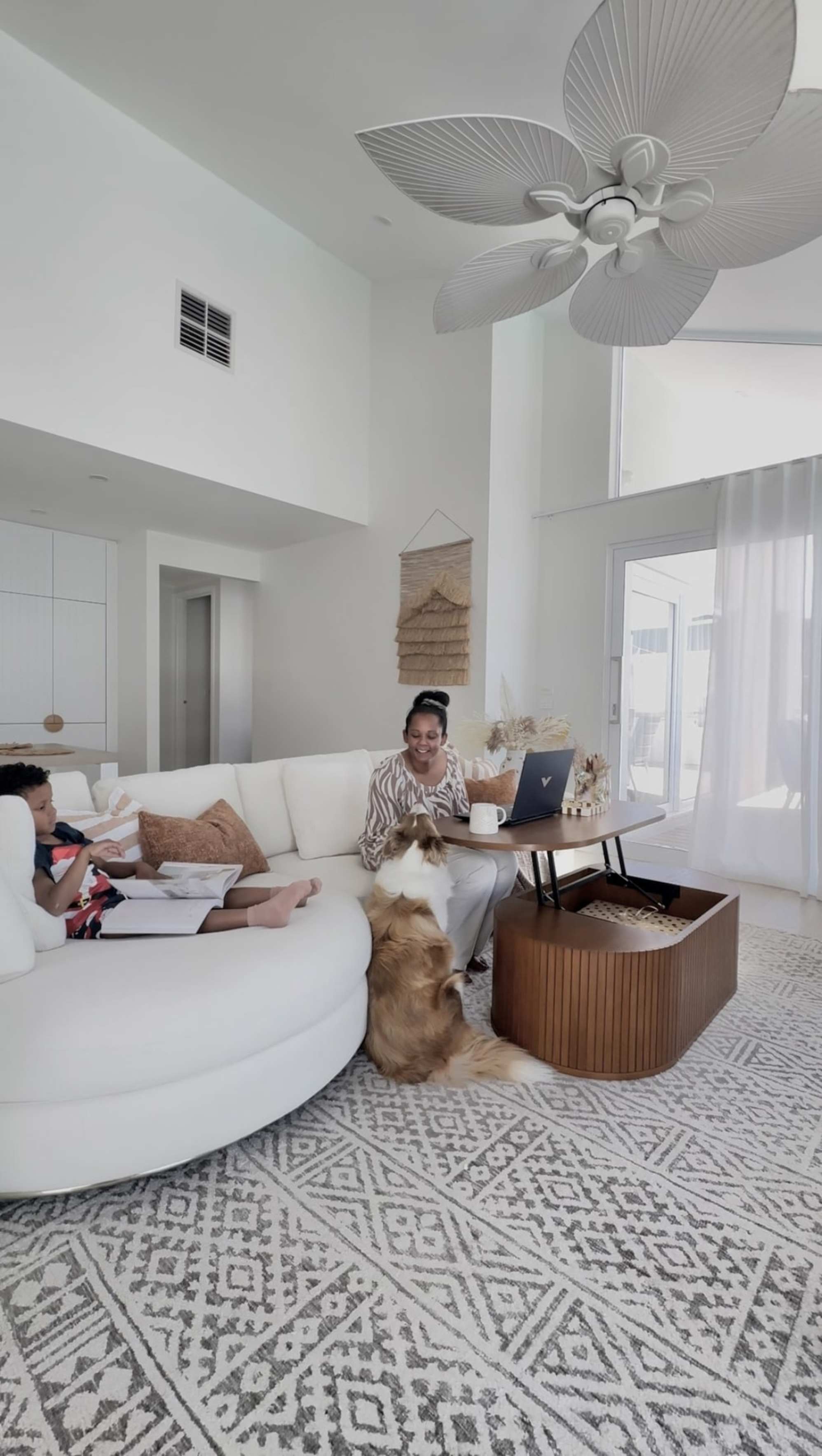 A person sitting on a round chaise sectional sofa while playing with their dog.