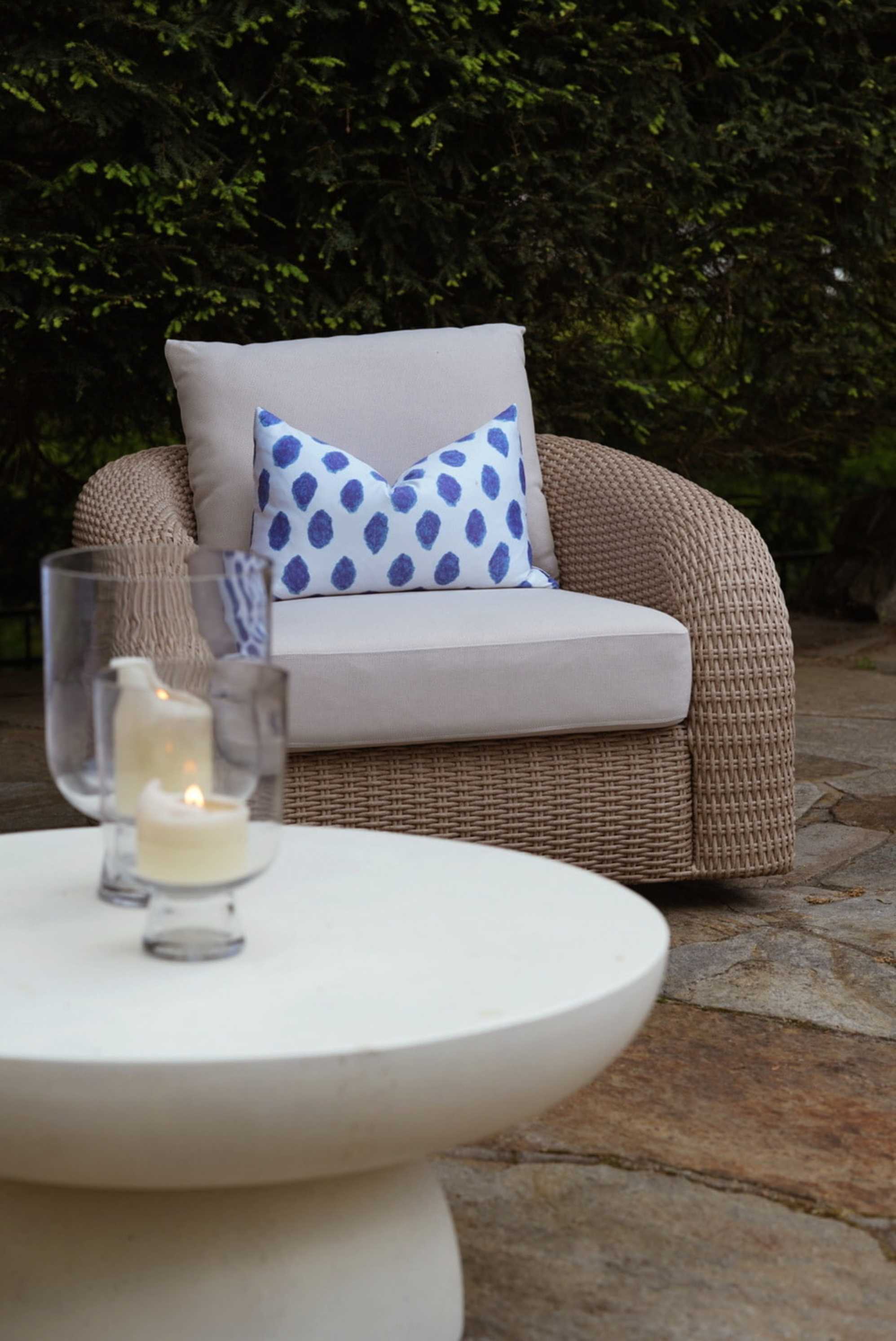 A wicker swivel chair and a white round coffee table placed outdoors.