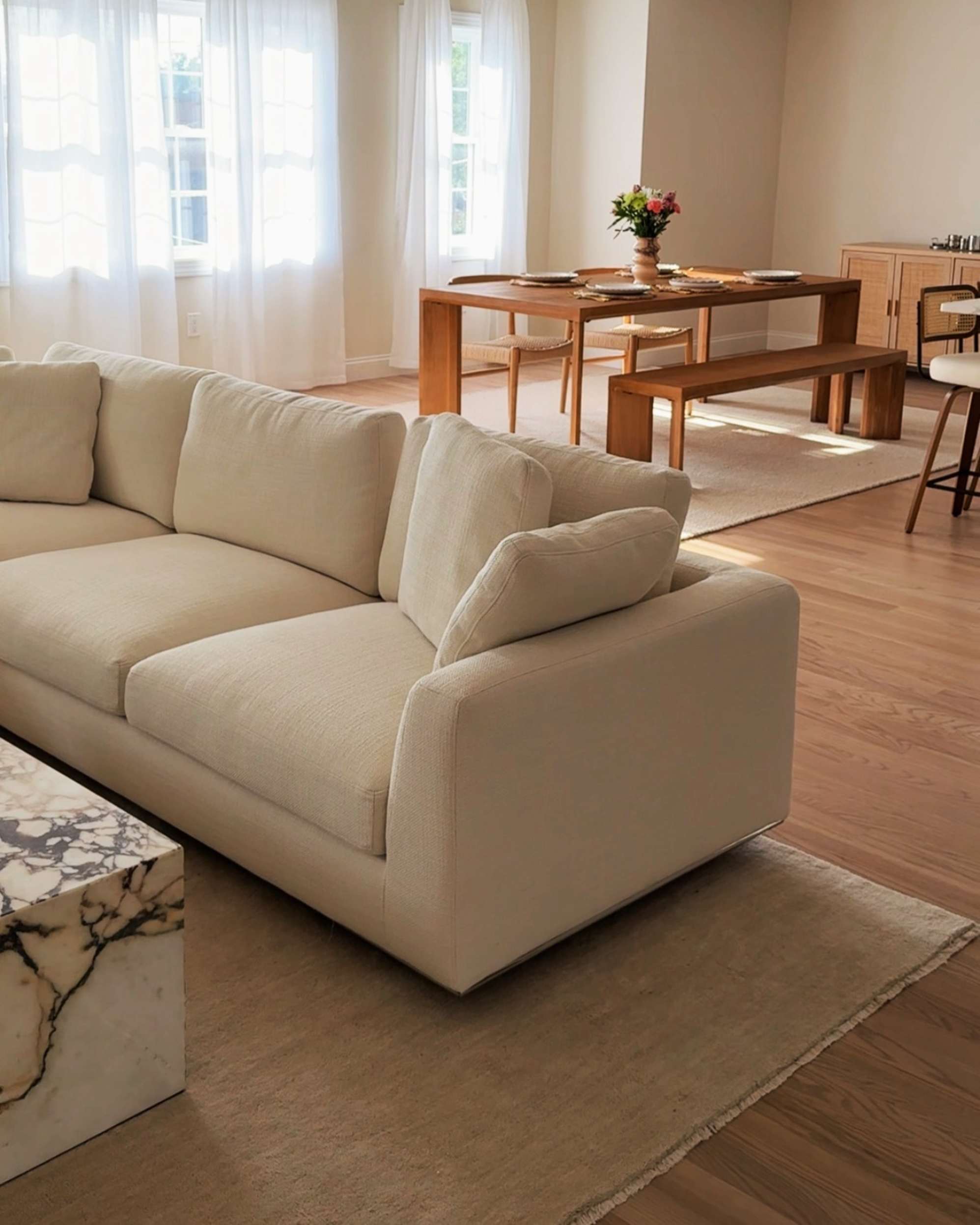 A chaise sectional sofa placed atop a wool area rug and the dining area behind it.