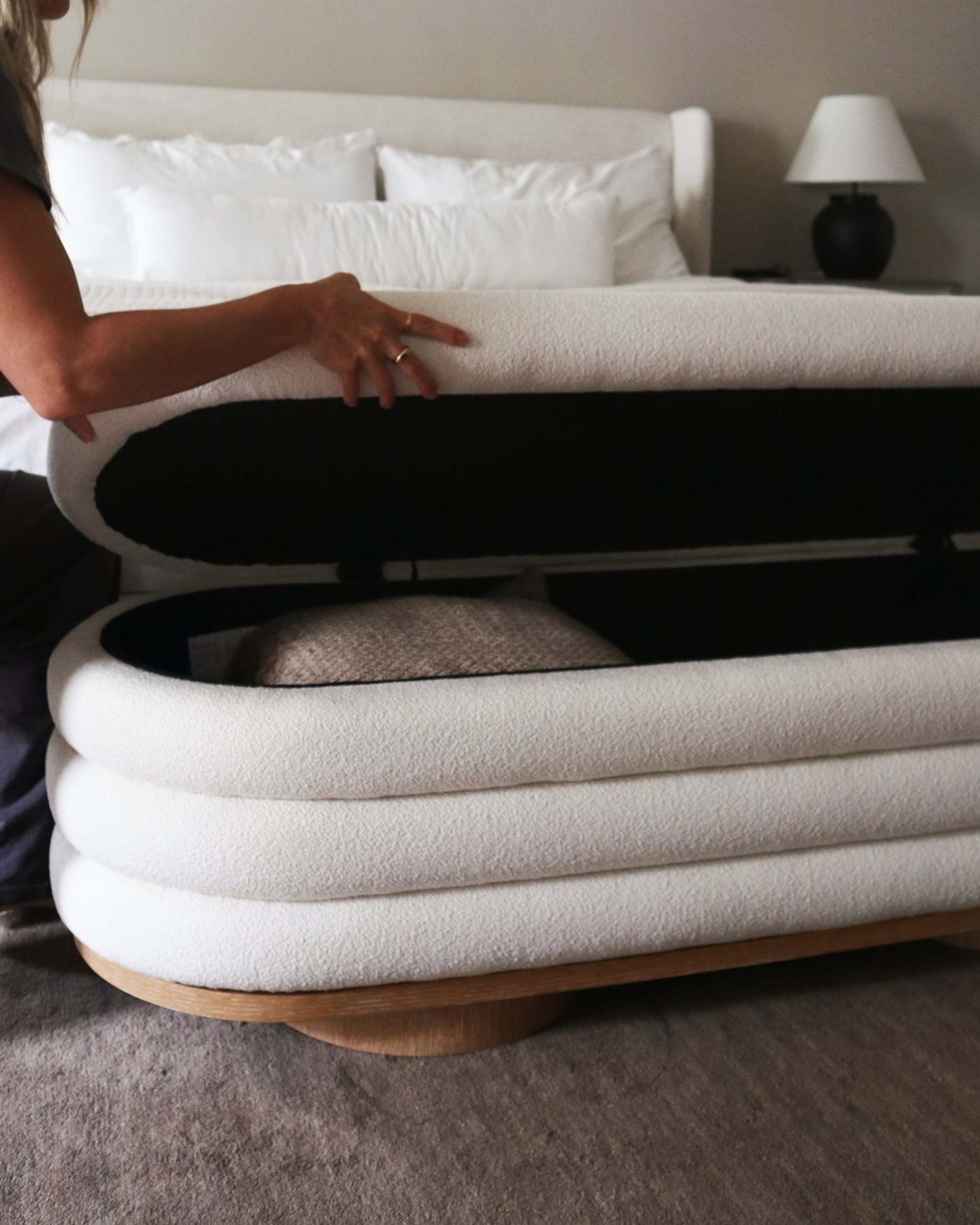 A person opening a storage bench to reveal a thick throw.