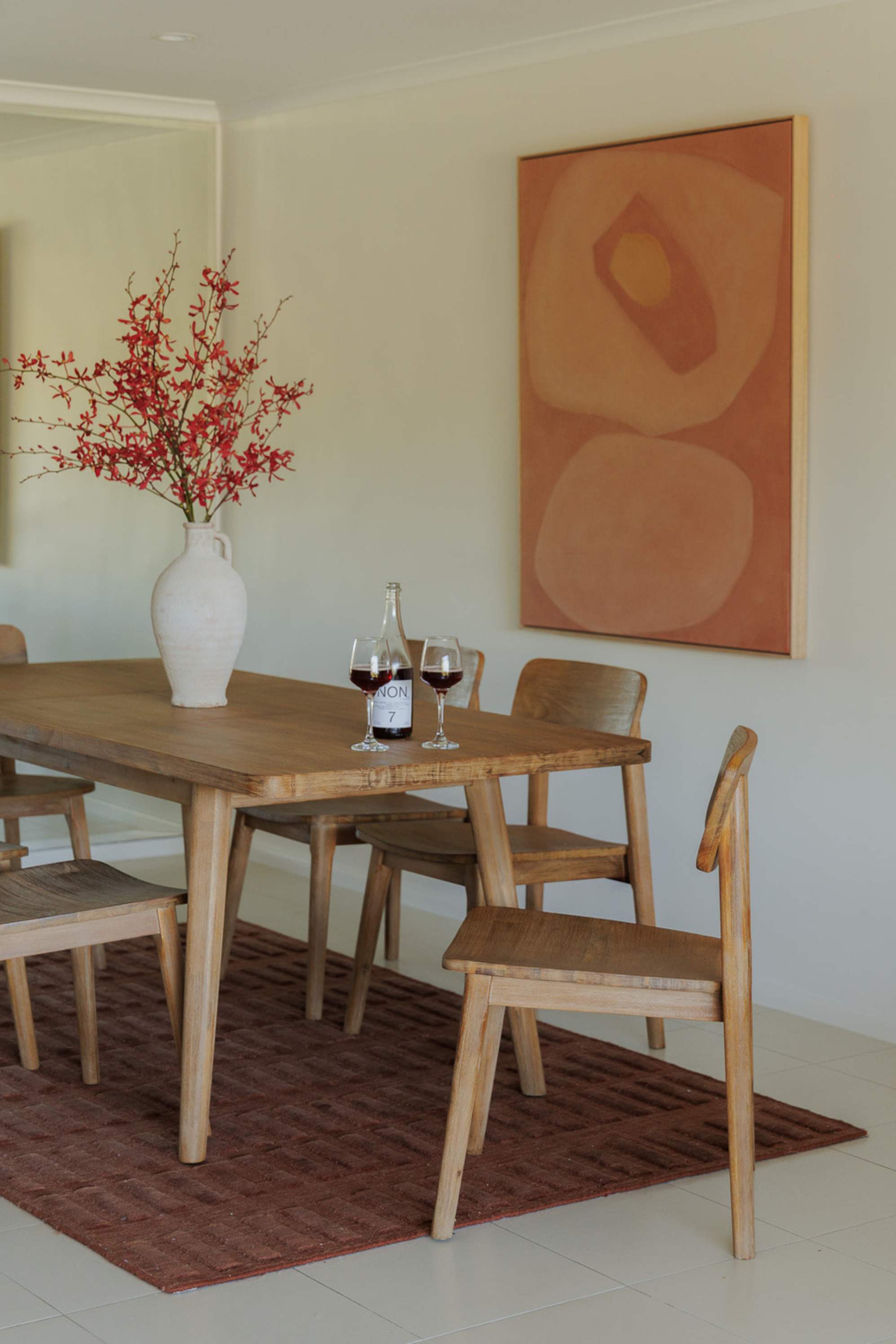 An acacia wood dining table set placed atop a wine red area rug.