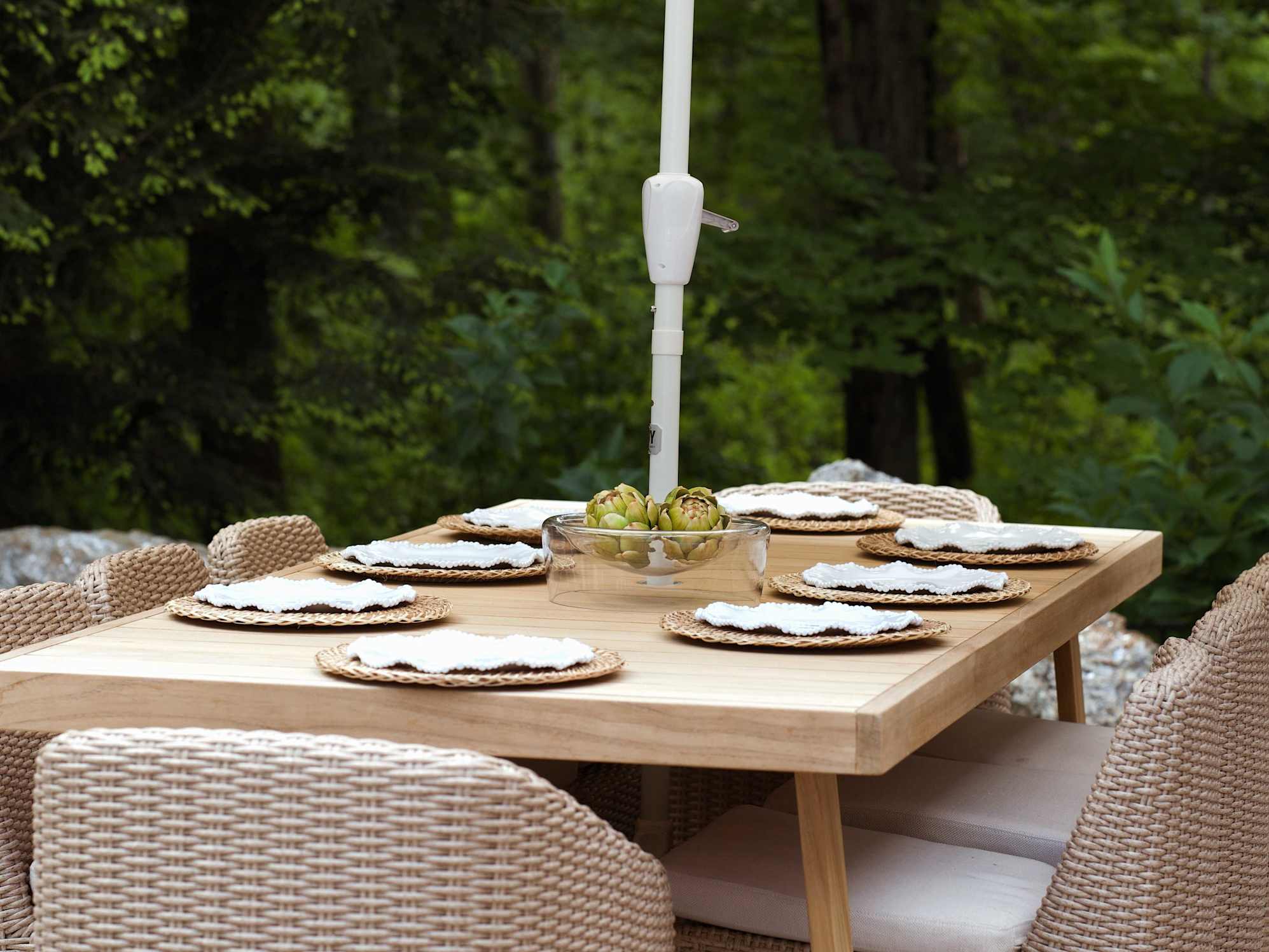  teak outdoor dining table with six wicker chairs and an outdoor umbrella.