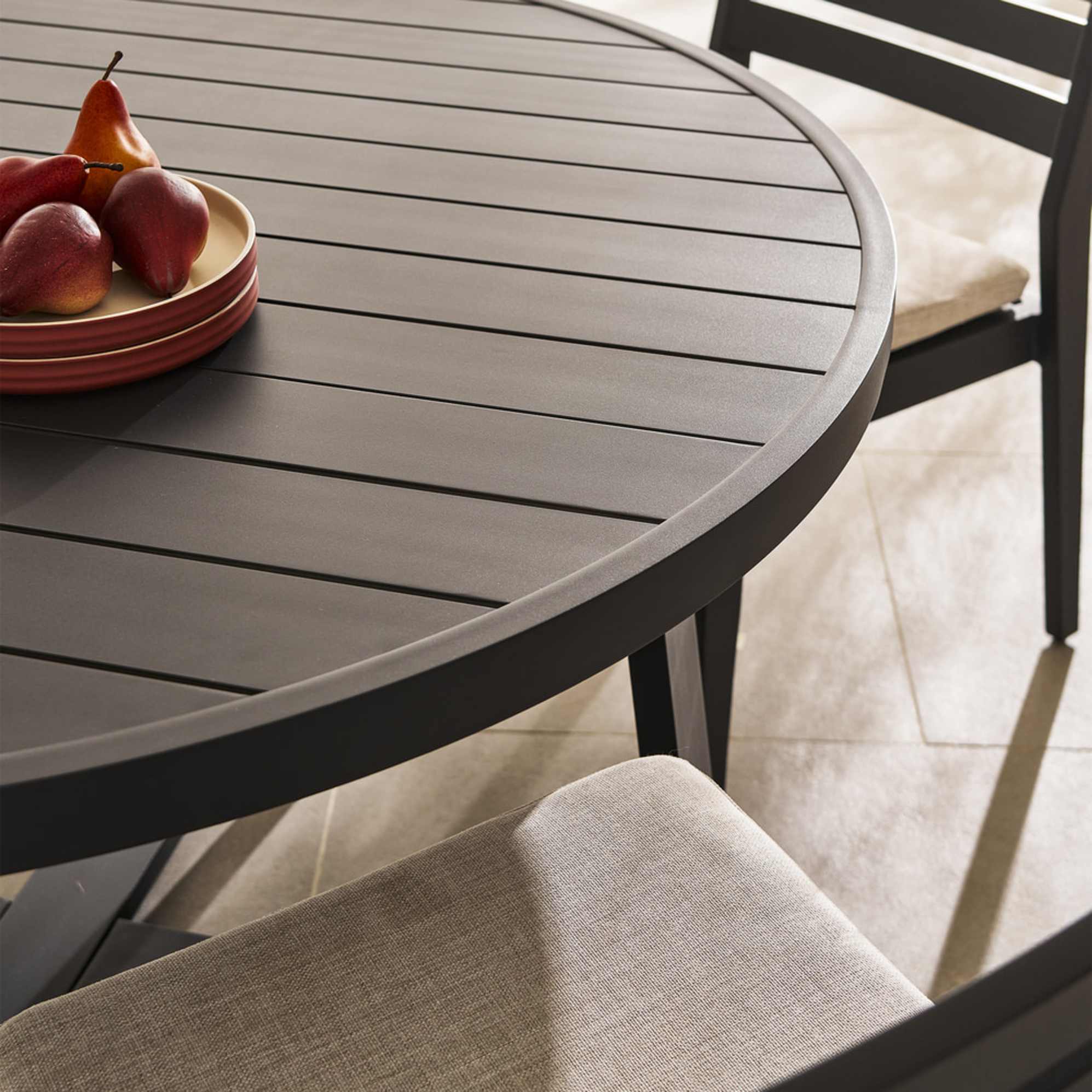 A round aluminum outdoor dining table with a plate of fruit placed in the center.
