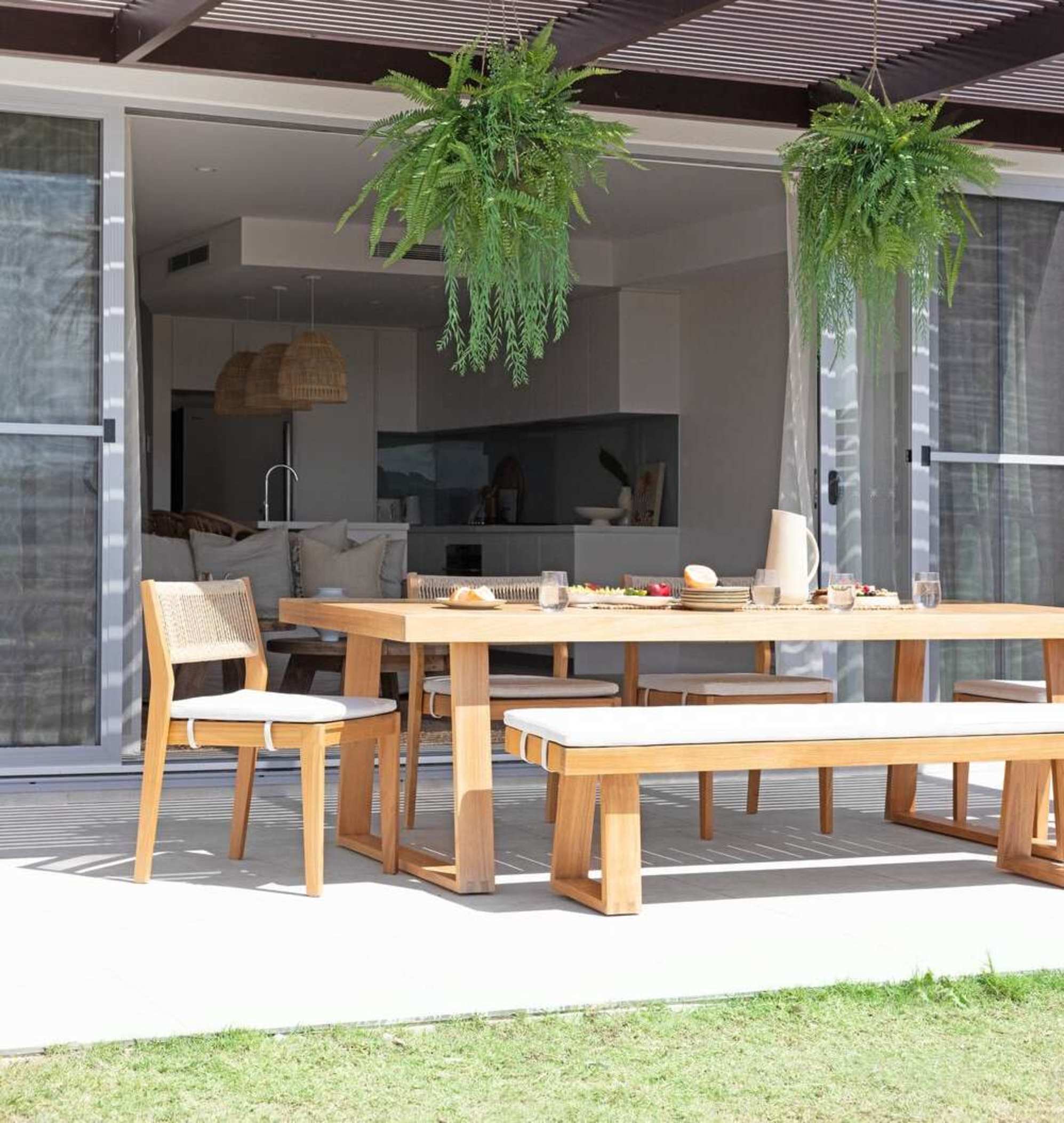 A teak dining table with a bench and 4 chairs sits on a patio. 
