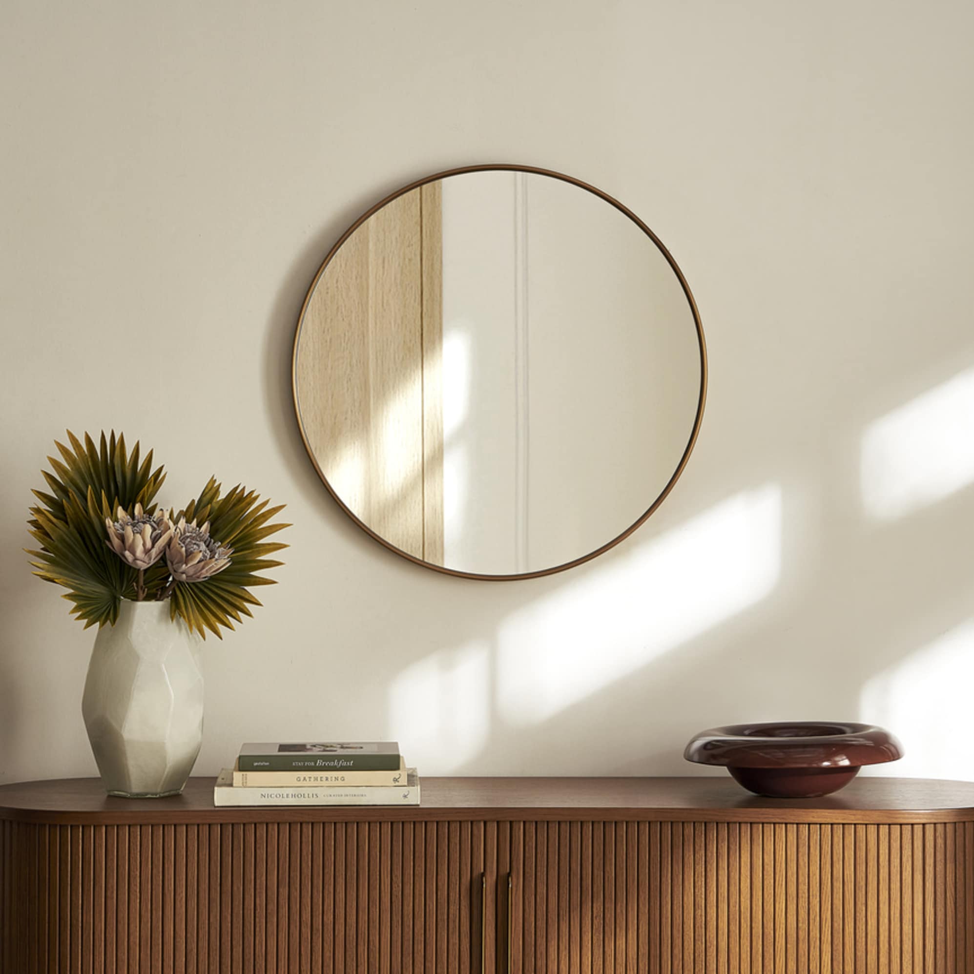 A round wall mirror hanging on a wall above a wooden sideboard.