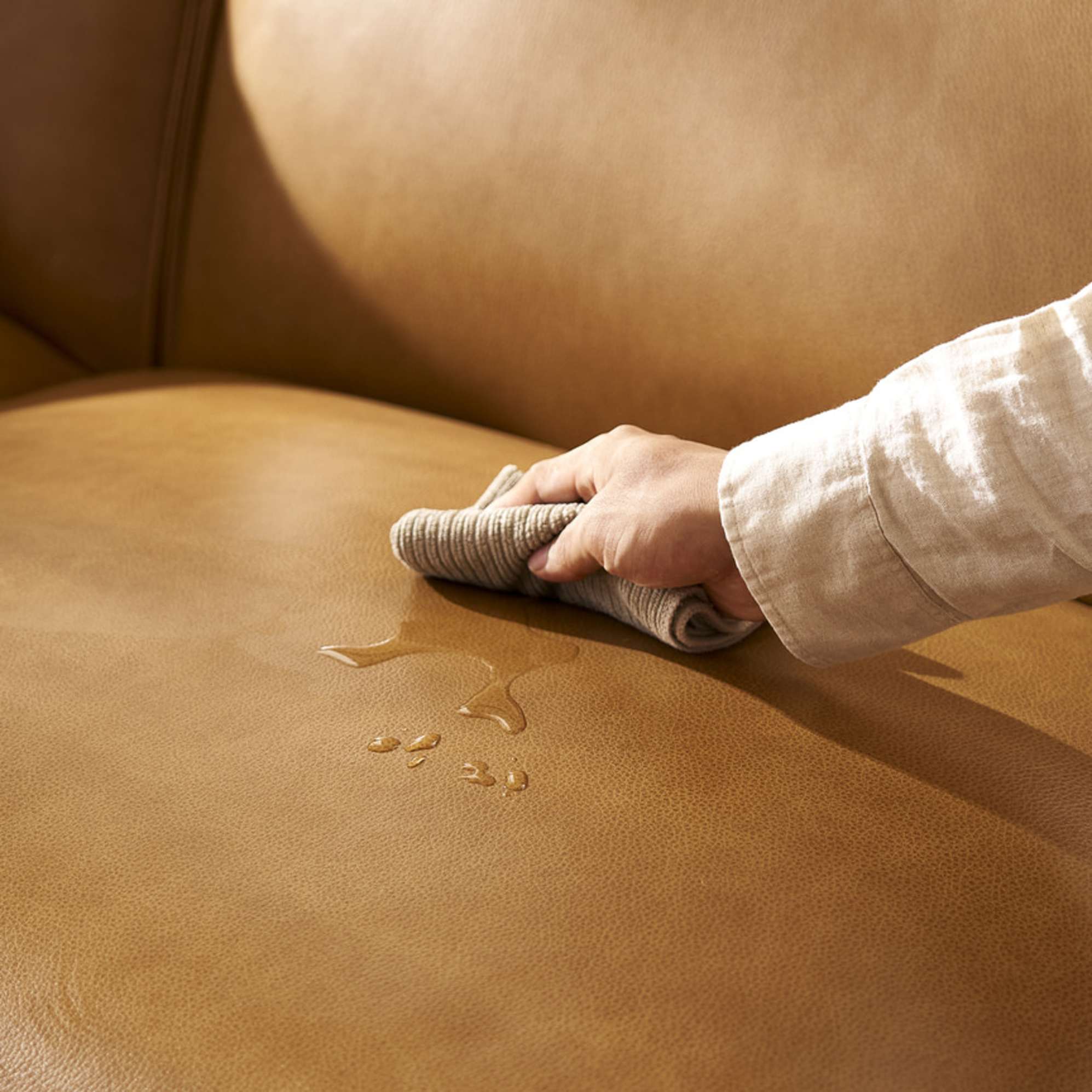 A person wiping a spill off a leather sofa.