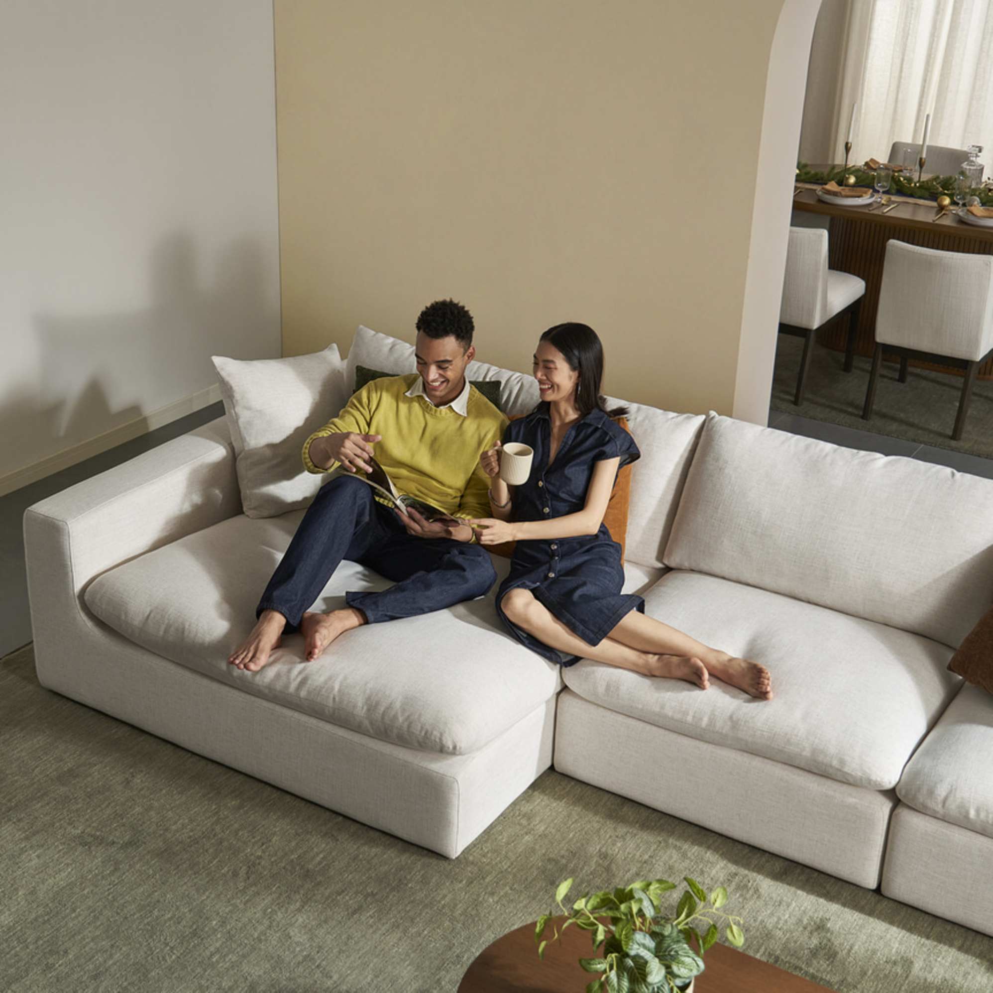 Two people seated on a wide chaise module of a sofa.