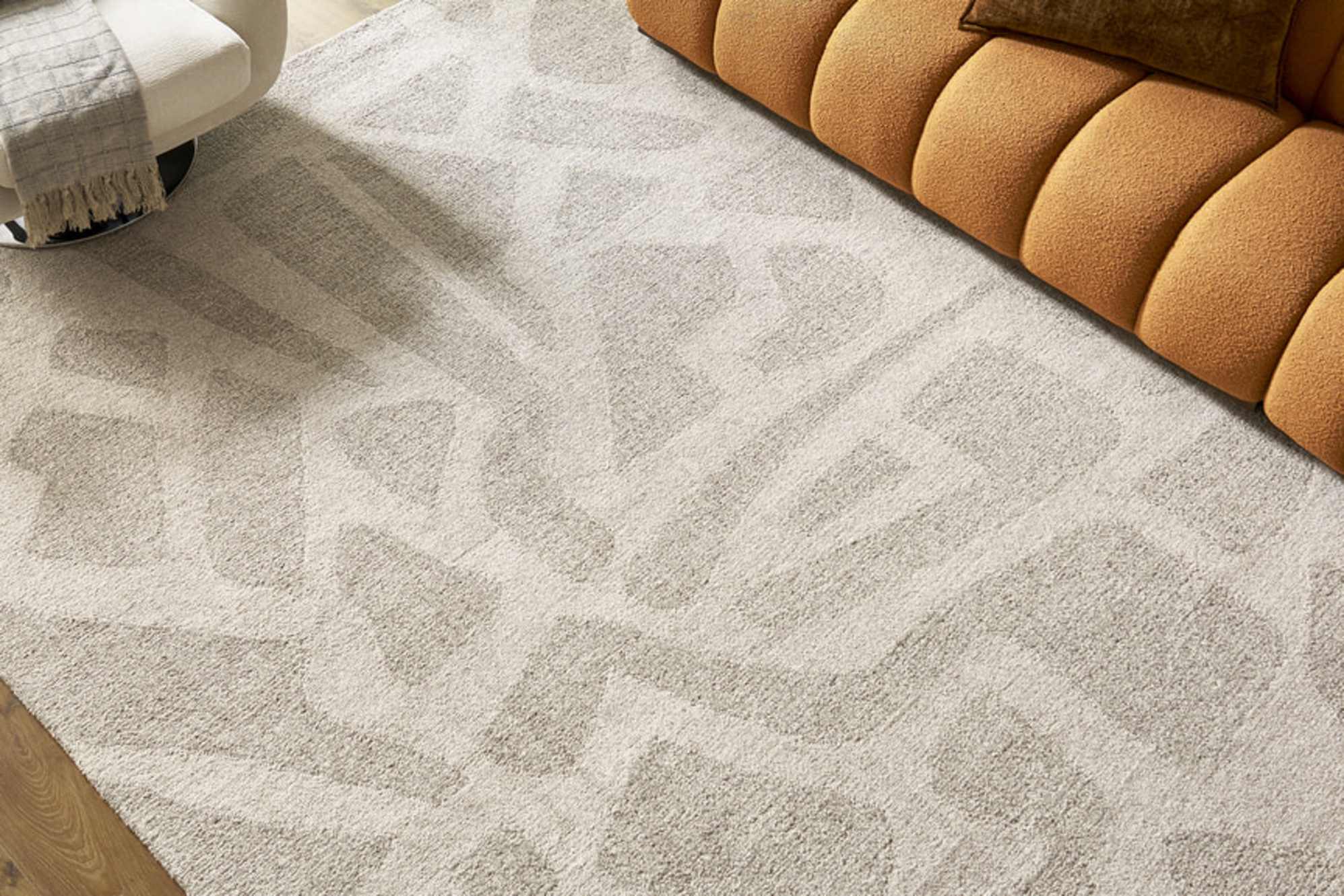 A rug with subtle geometric patterns placed beneath a rust colored sofa.