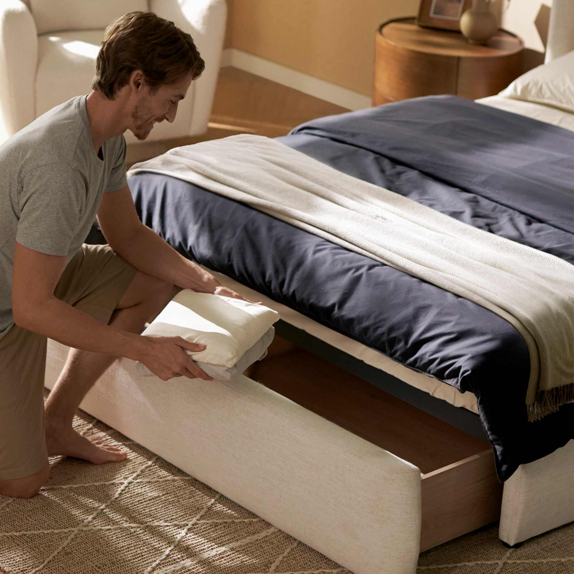 A person placing linen in the drawer storage under a bed.