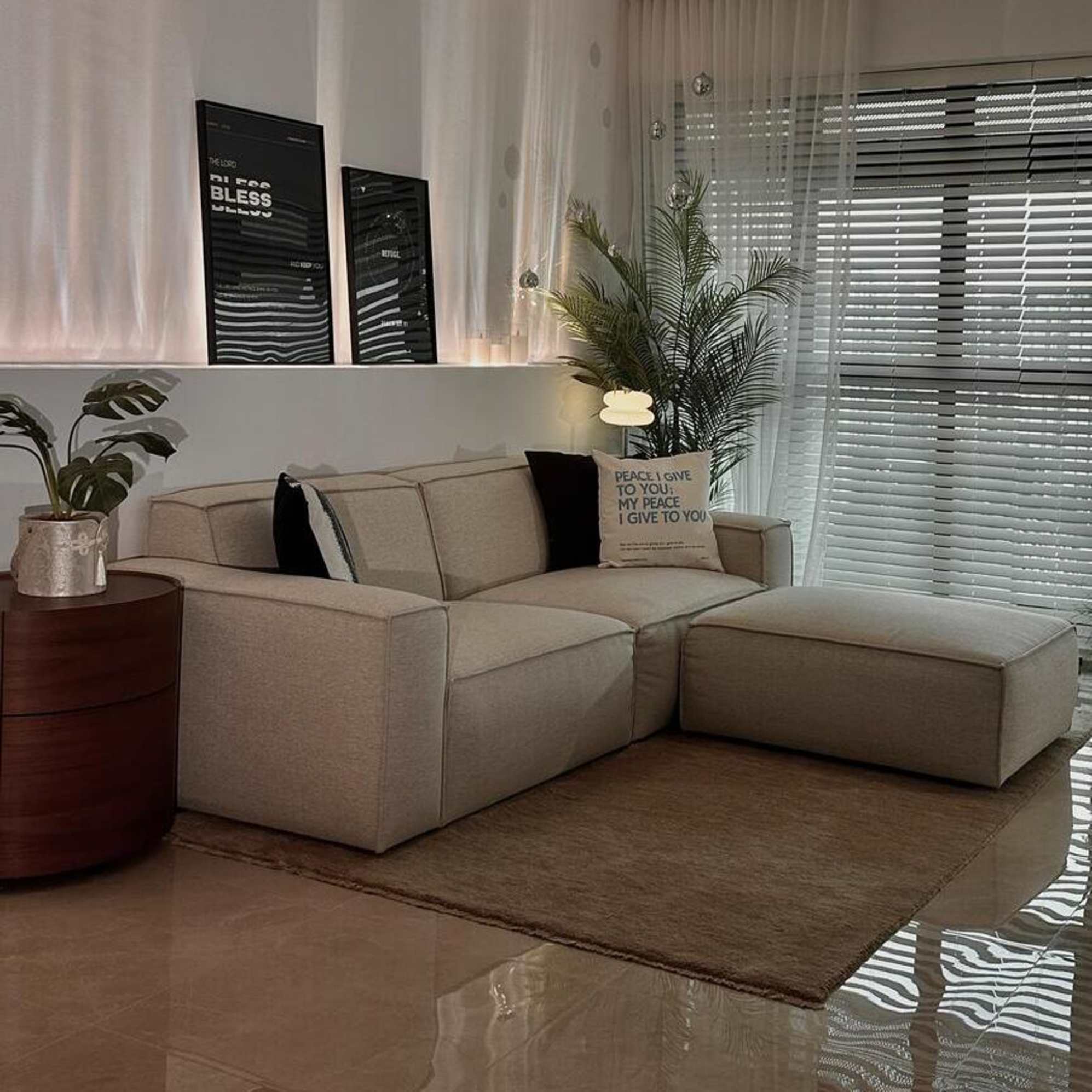 A 2-seater sofa with a matching ottoman placed on top of a wool area rug with a wooden side table beside it.