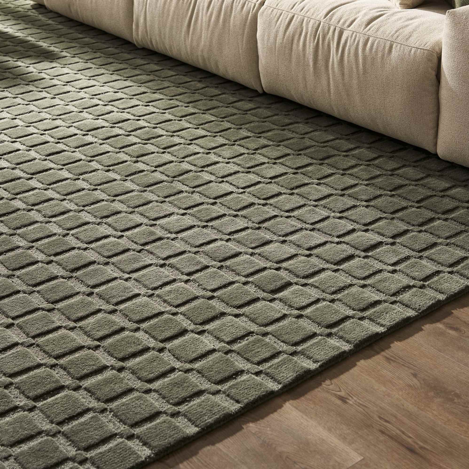 A dark green area rug with raised square patterns placed beneath a sofa.