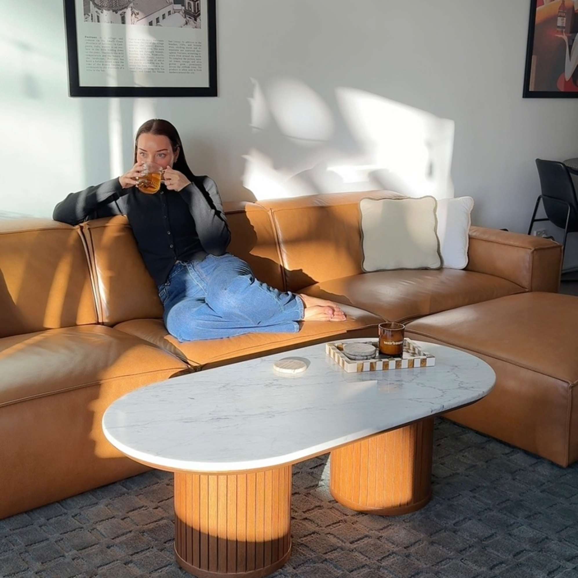 A person sitting on a leather sofa while drinking from a mug.