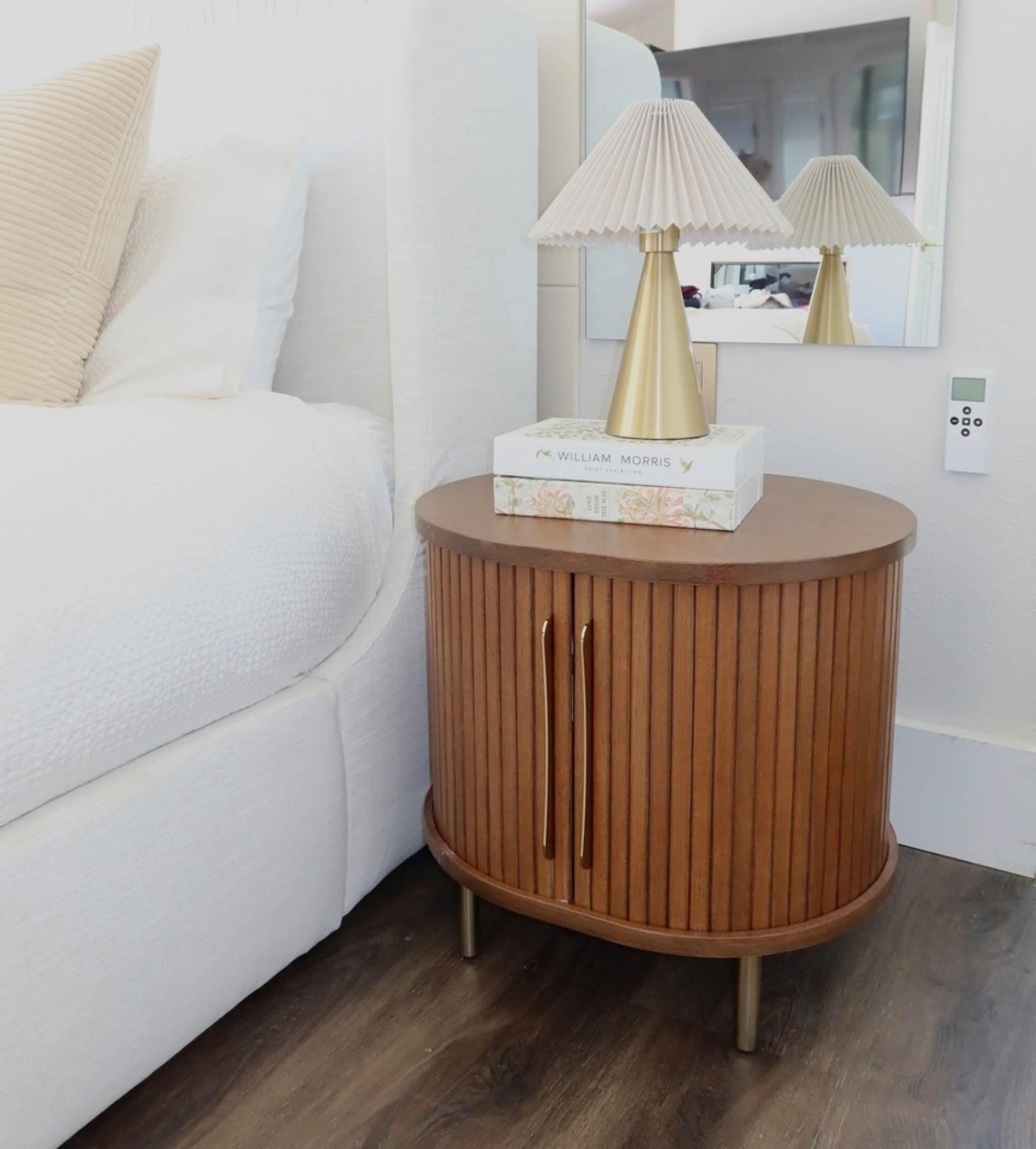 A wooden nightstand with tambour details with a lamp placed atop.