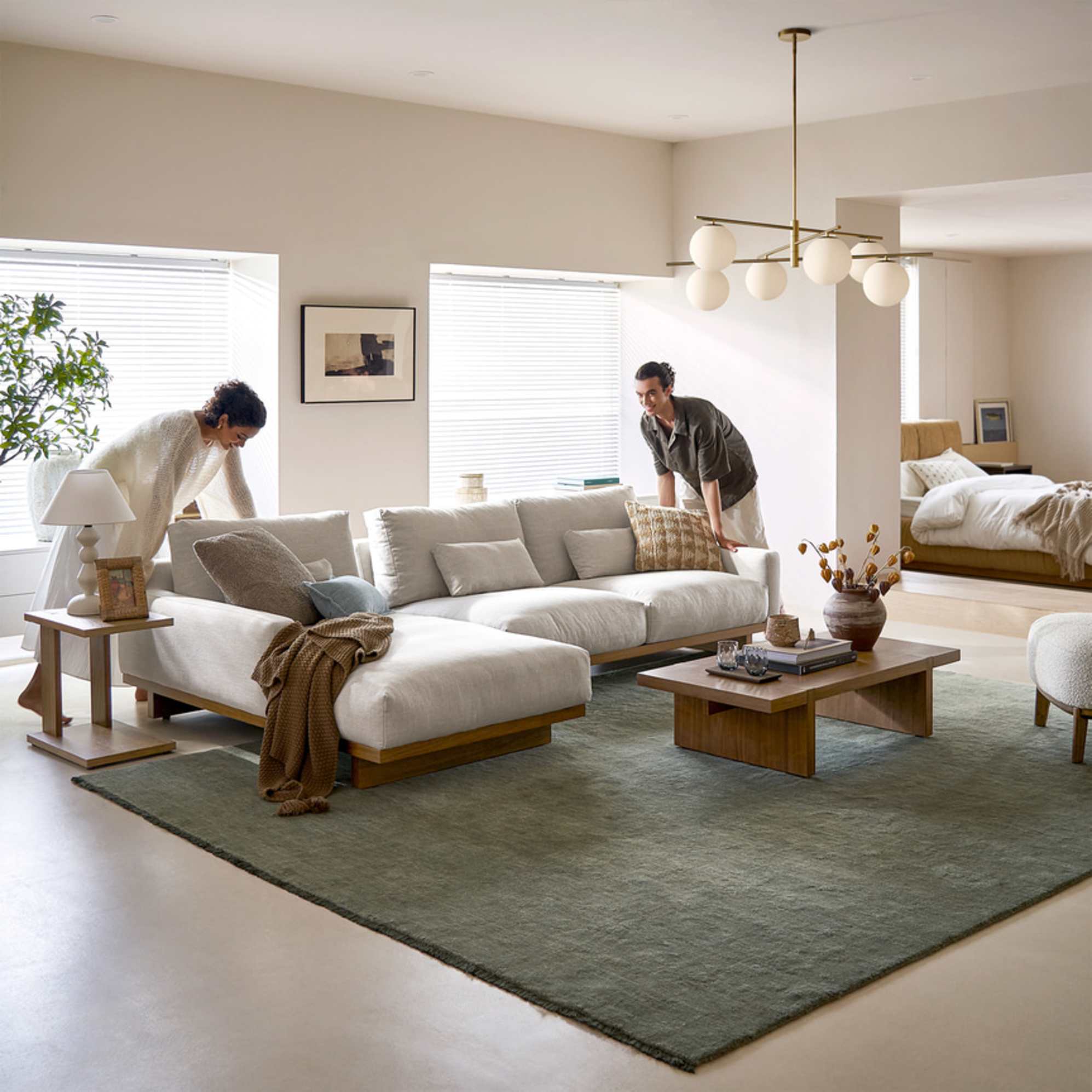 Two people arranging a modular performance fabric chaise sectional sofa.
