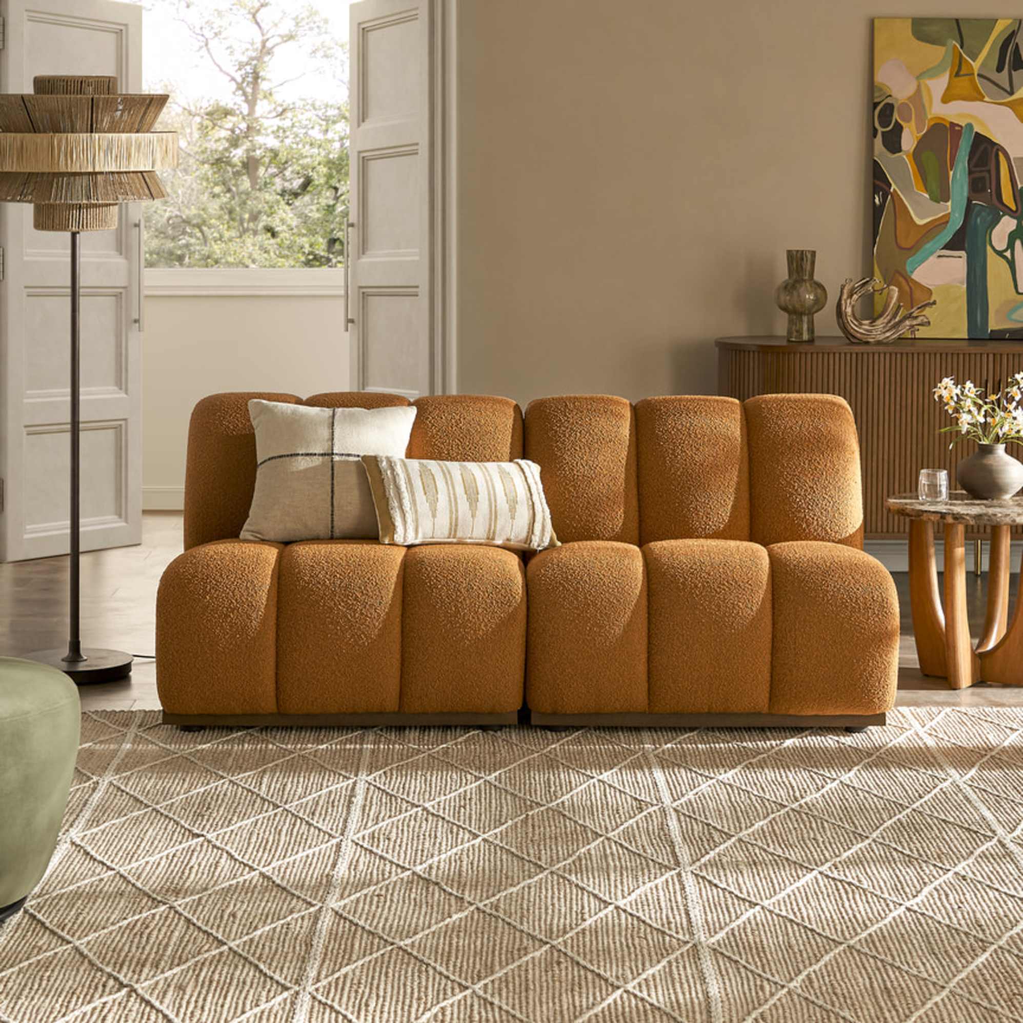 A copper-colored 2-seater sofa with channel tufting placed in a living room on a jute rug.