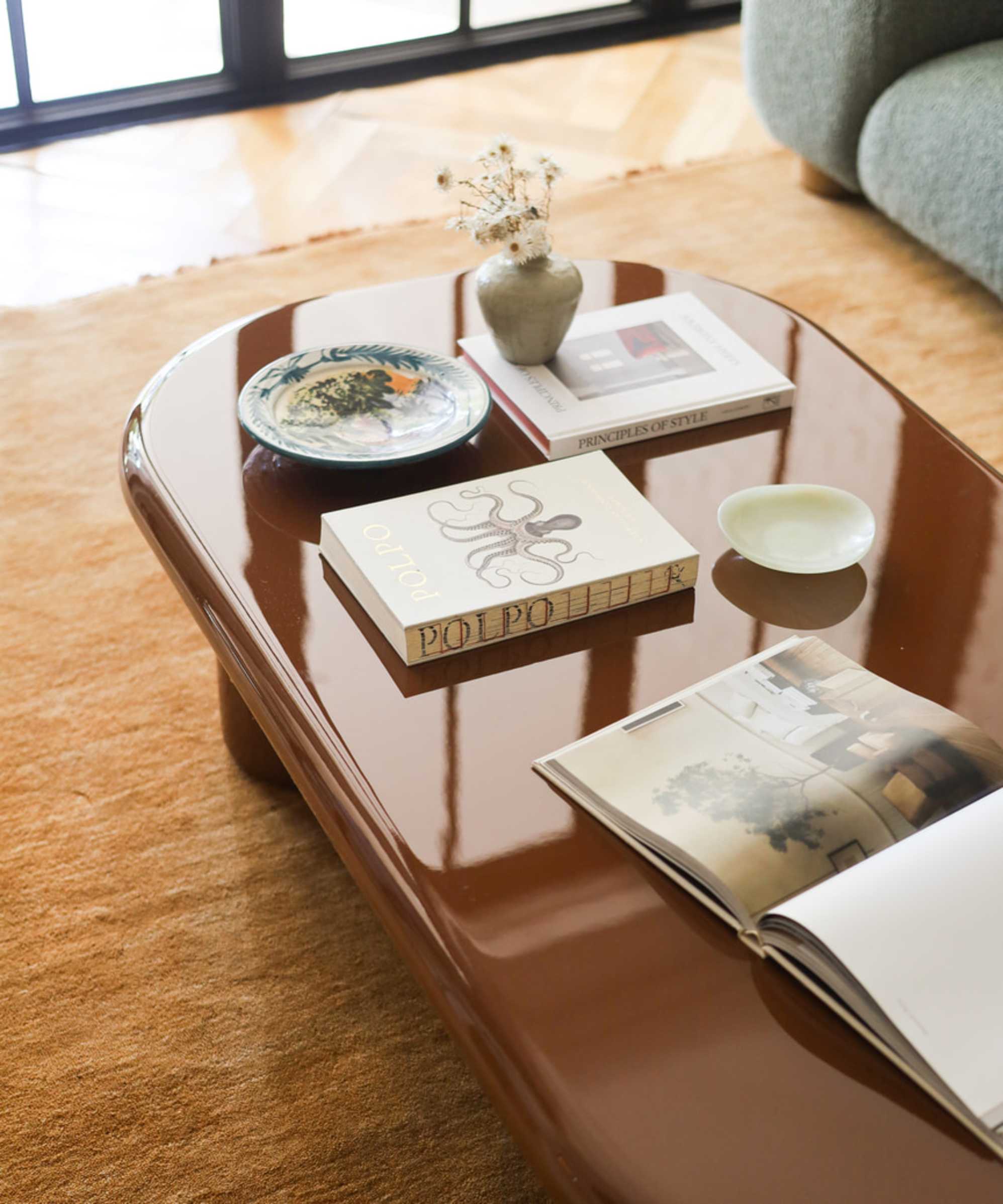 A brown coffee table that features a glossy finish with books and magazines placed on its surface.