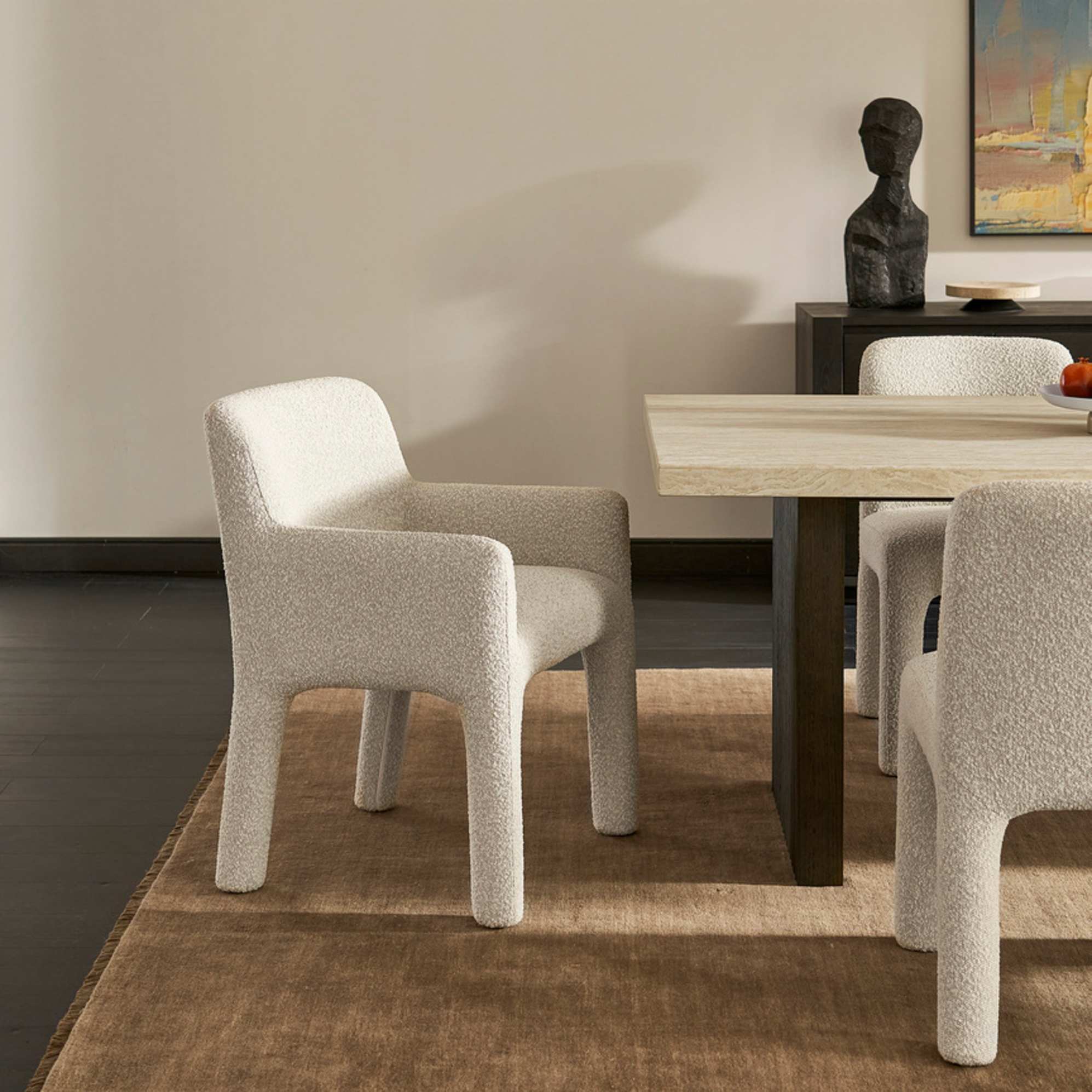 A performance bouclé dining armchair placed in front of a travertine dining table.