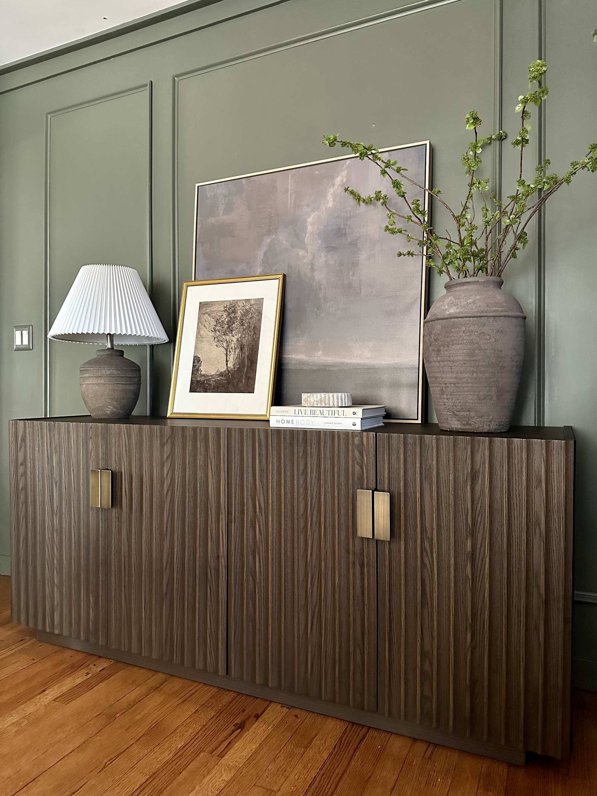 A wooden TV console nicely decorated with plants, a lamp and paintings.