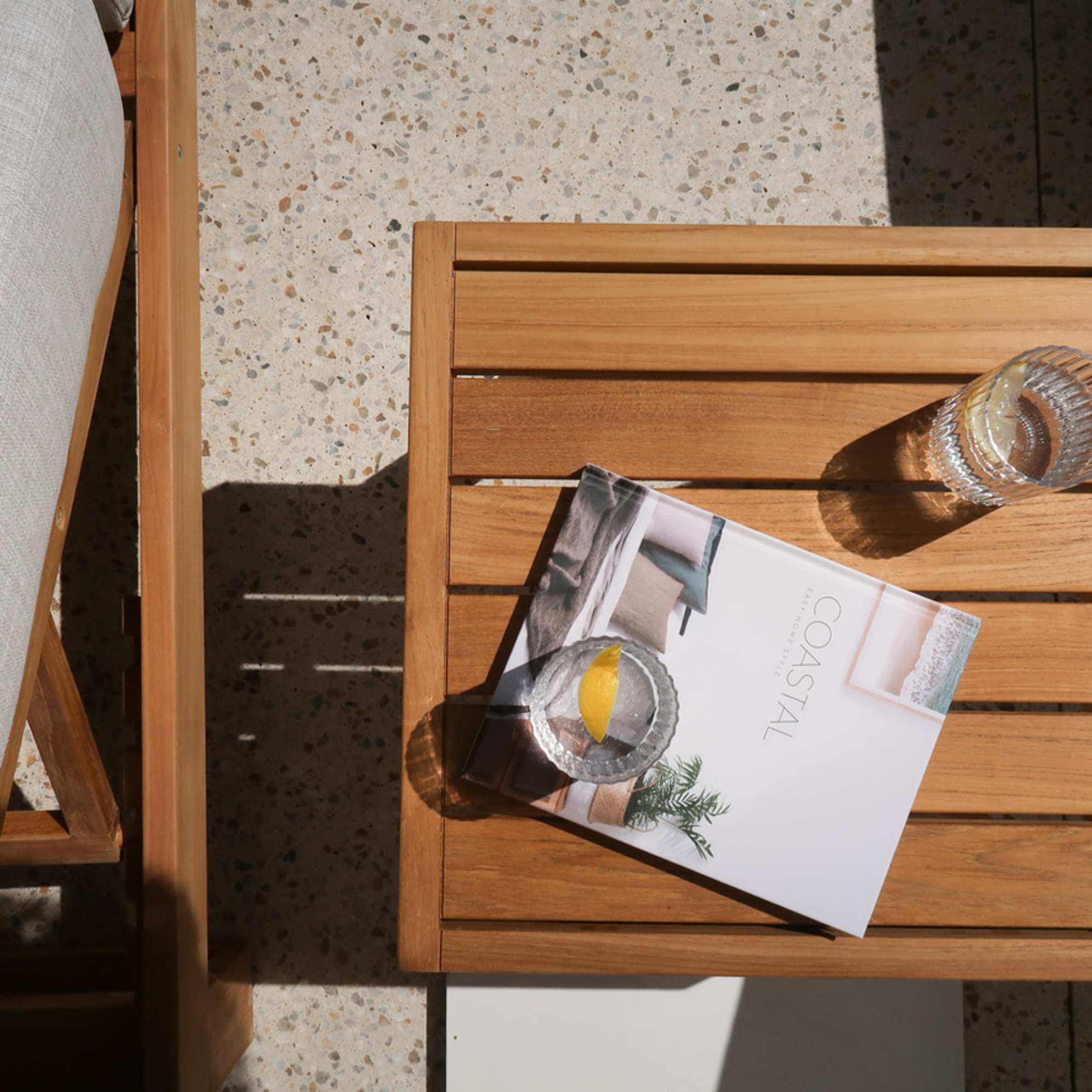 A teak wood side table placed by a pool deck with two glasses of water.